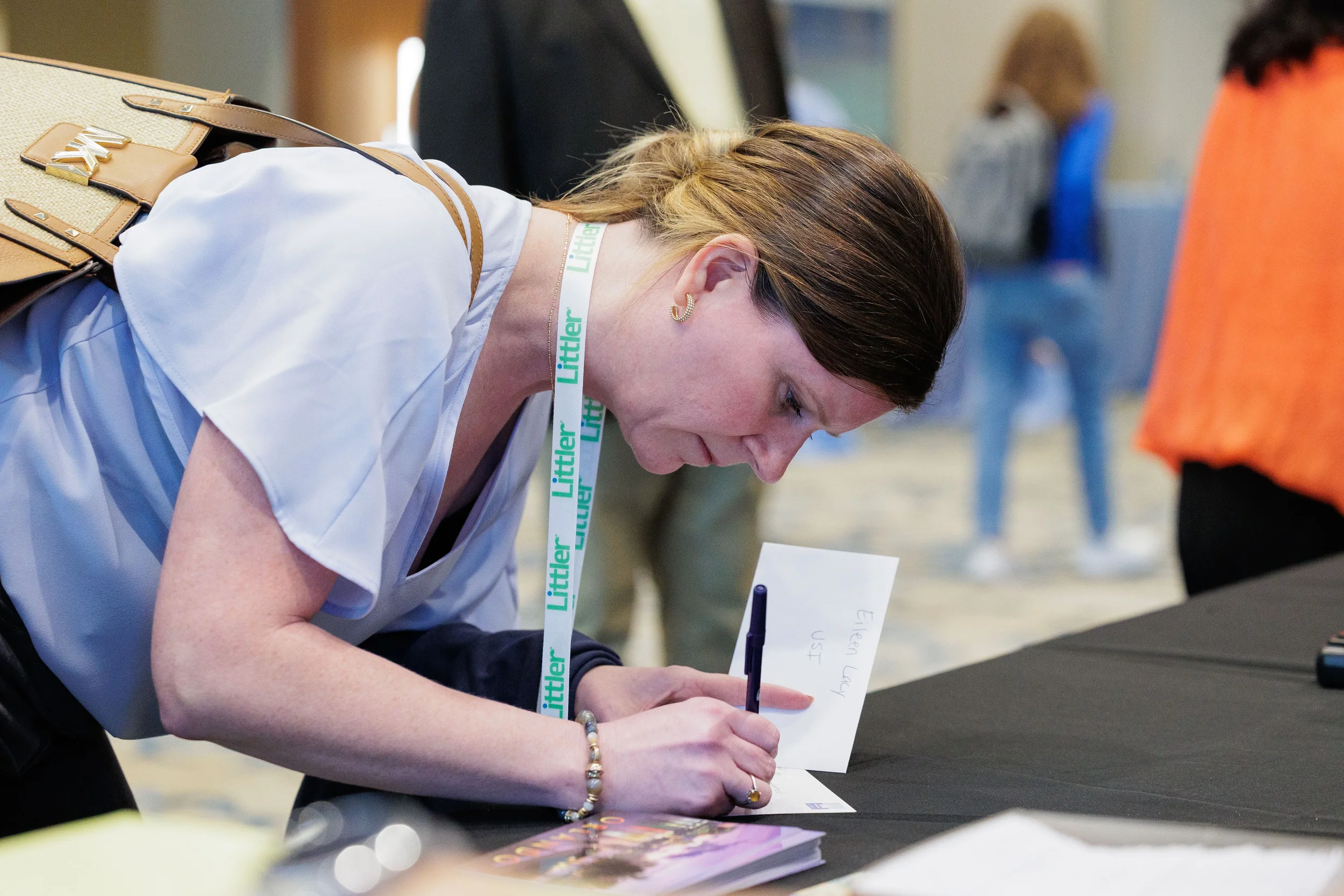 Attendee with lanyard leans over table writing at Chicago corporate conference registration area
