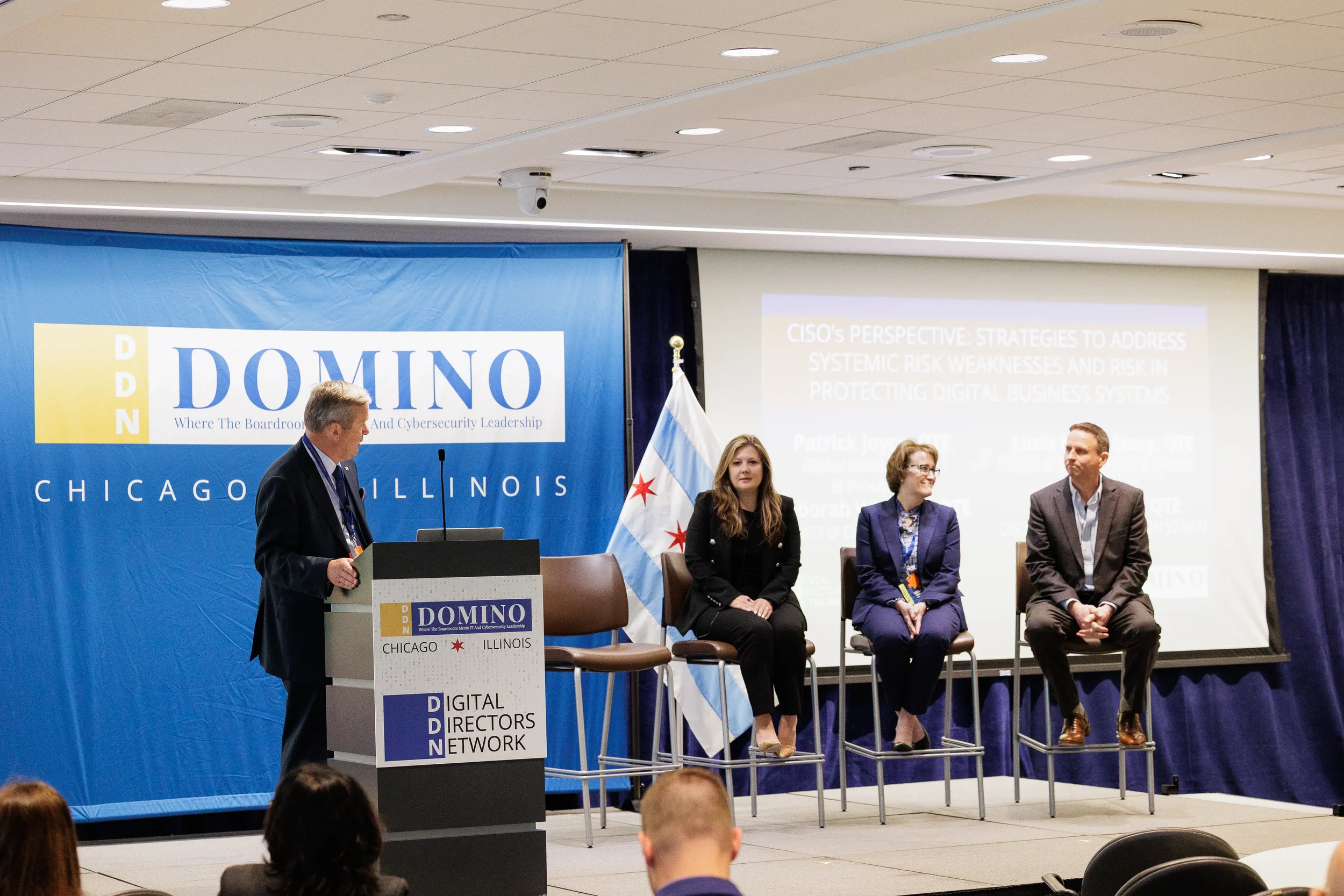 Moderator at podium with three panelists on branded stage with Chicago flag at Chicago corporate event