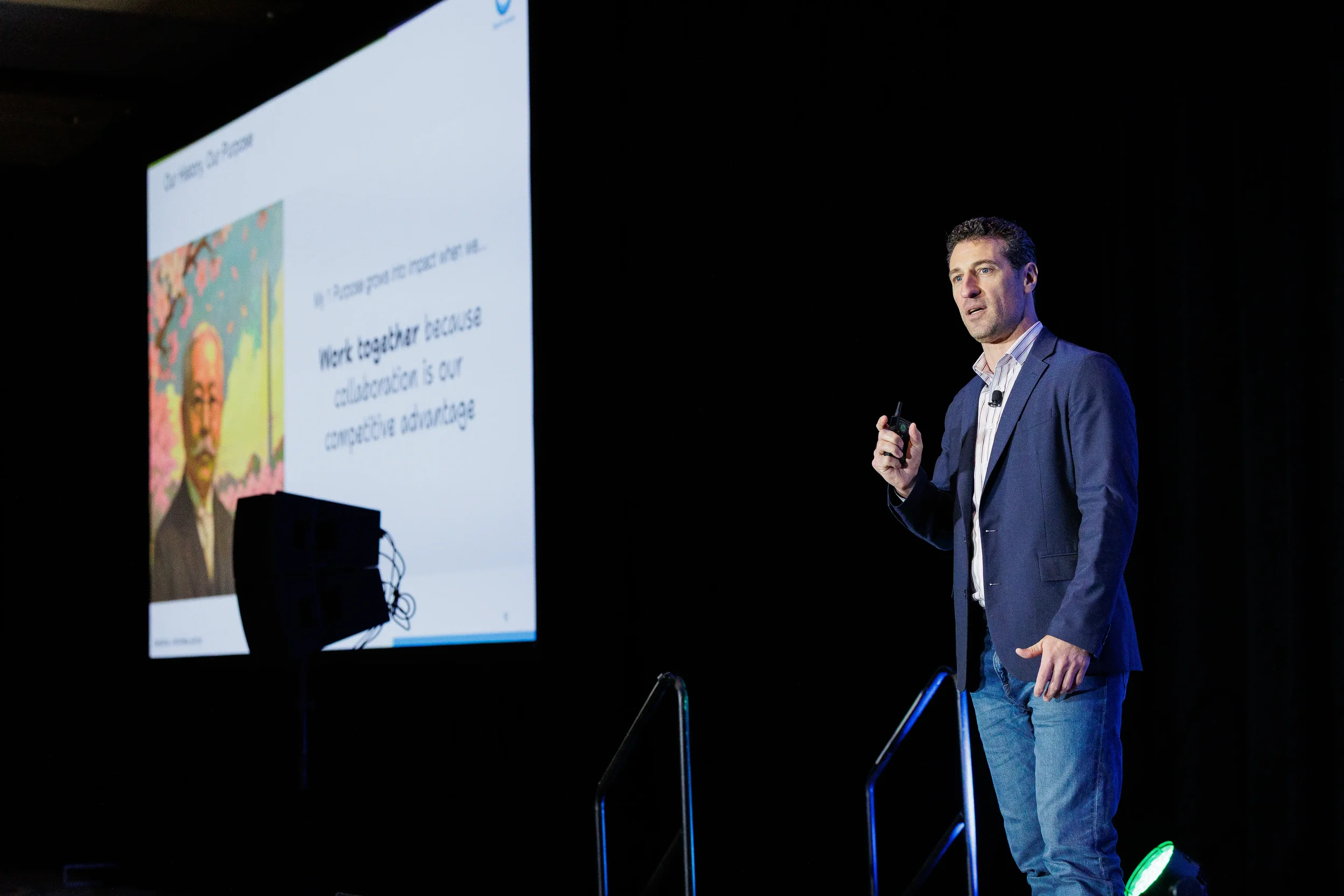 Speaker holds slide clicker while presenting on stage beside projection screen at Orlando corporate event