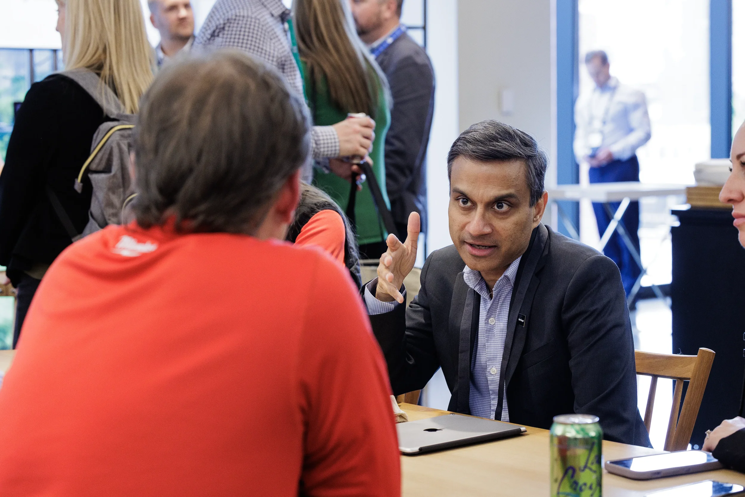 Attendee gestures while talking with colleagues at table during Orlando corporate networking break