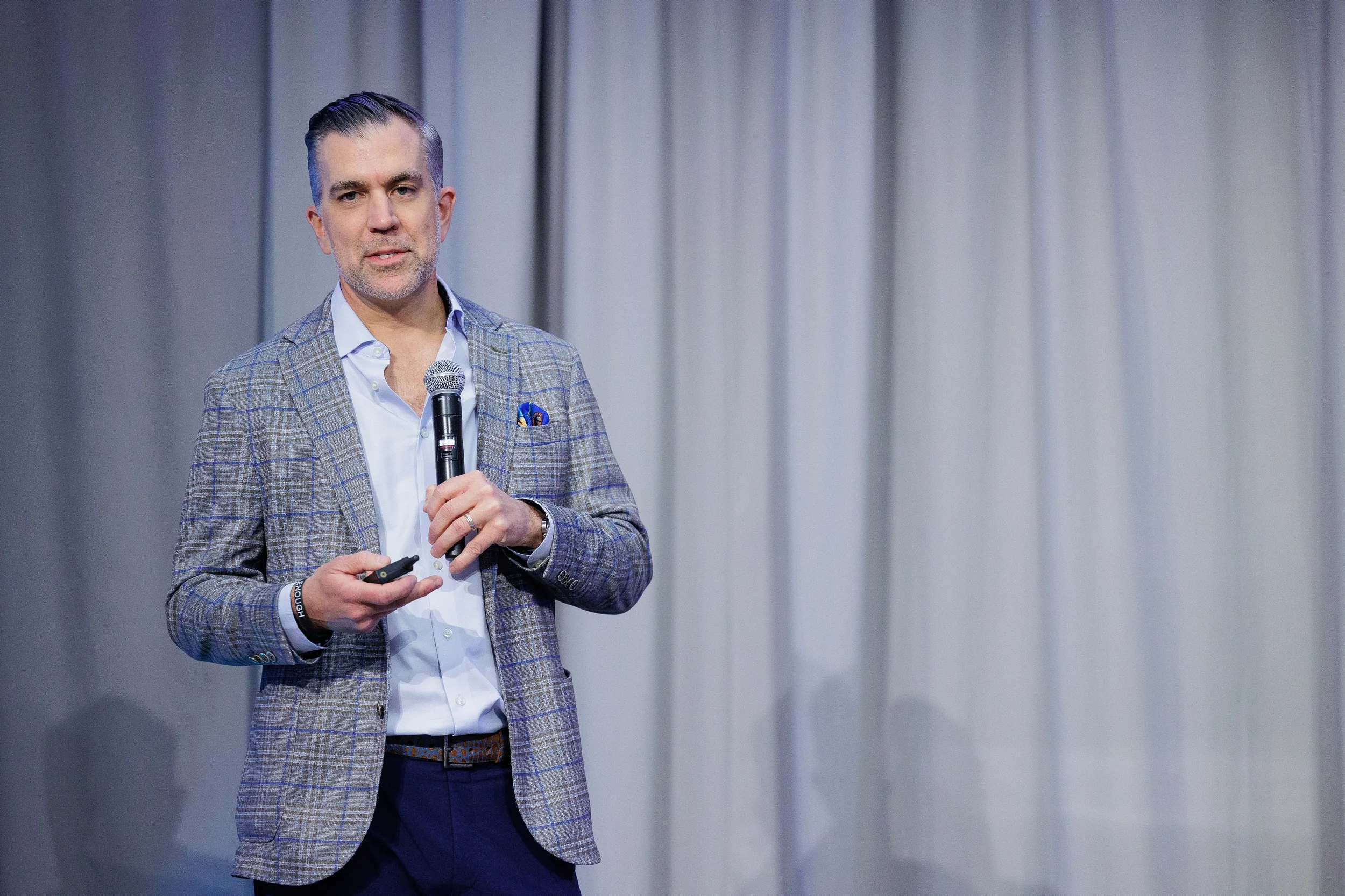Keynote speaker in plaid blazer holds microphone while presenting on stage at Chicago corporate event