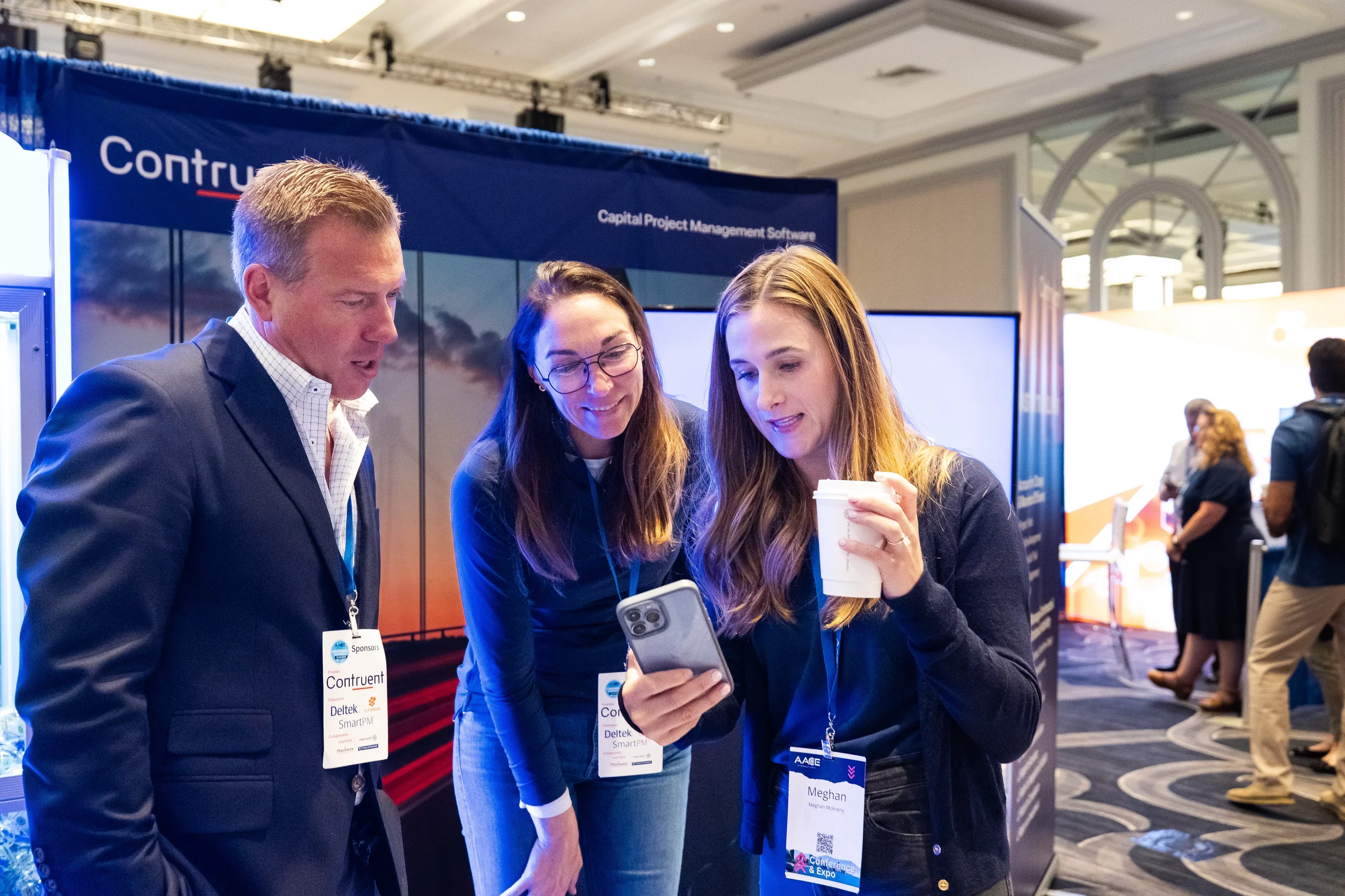 Exhibitors share phone screen with attendee at Contruent booth during AACE conference expo in Chicago