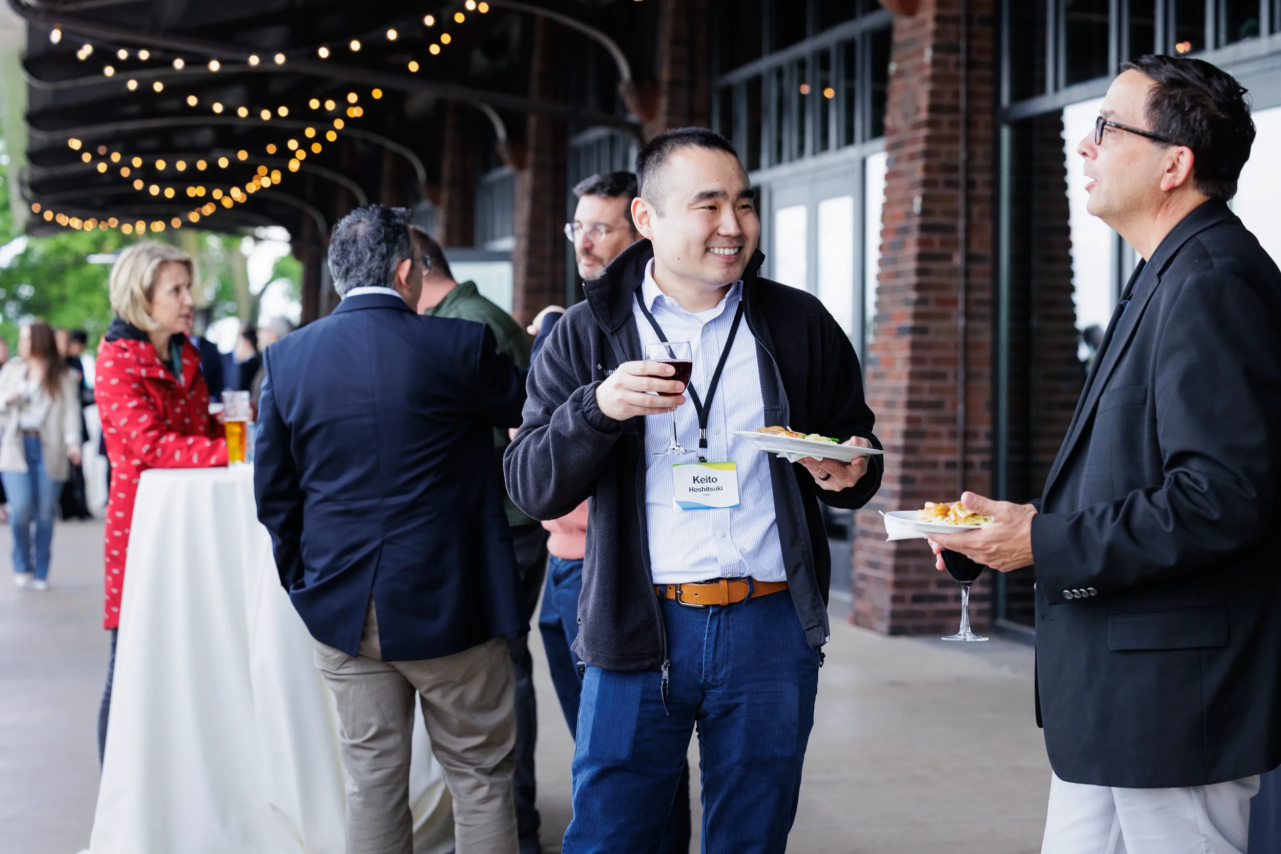 Attendees chat with food and wine under string lights at outdoor networking reception in Orlando