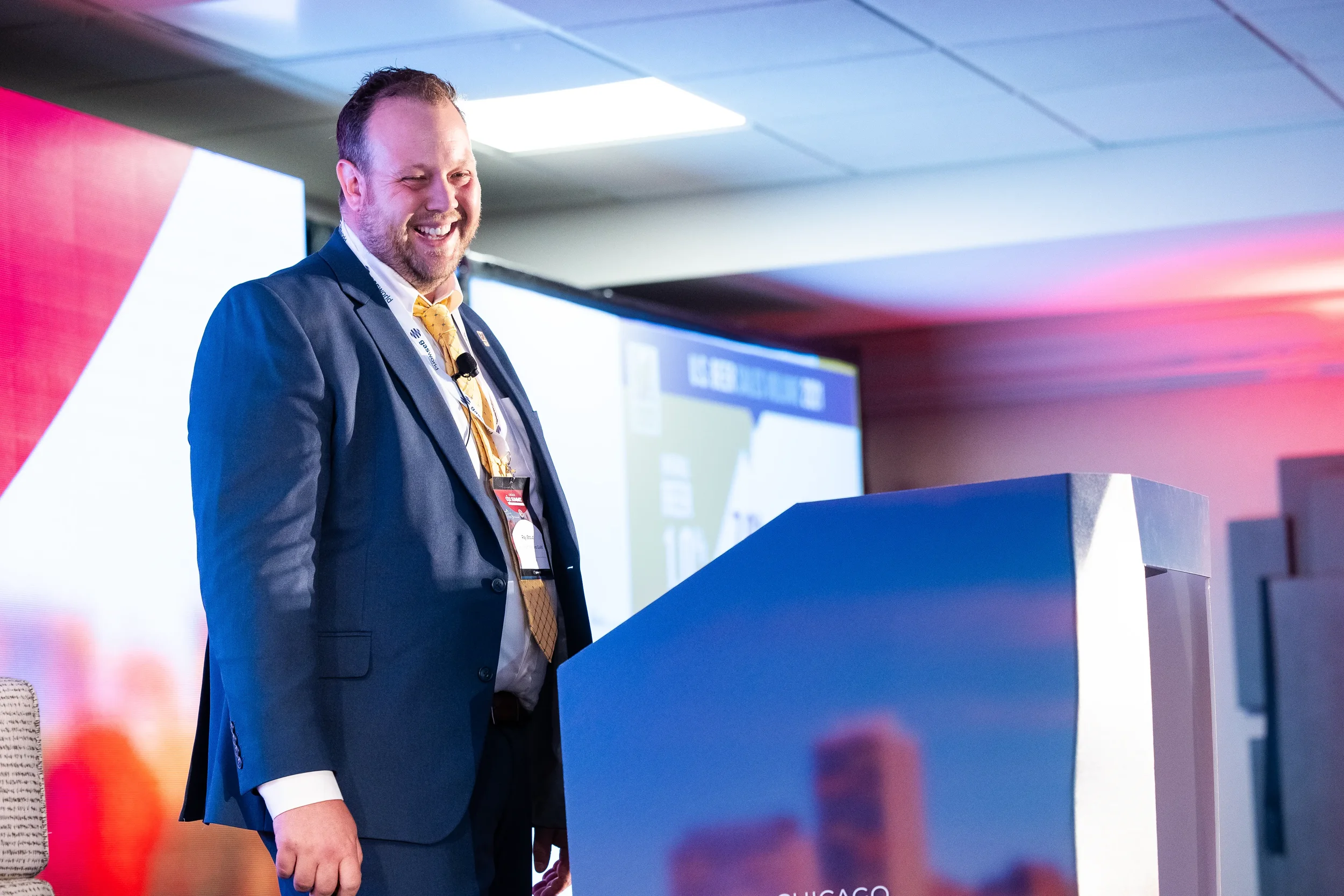 Keynote speaker laughs while presenting from podium on stage at Orlando industry conference