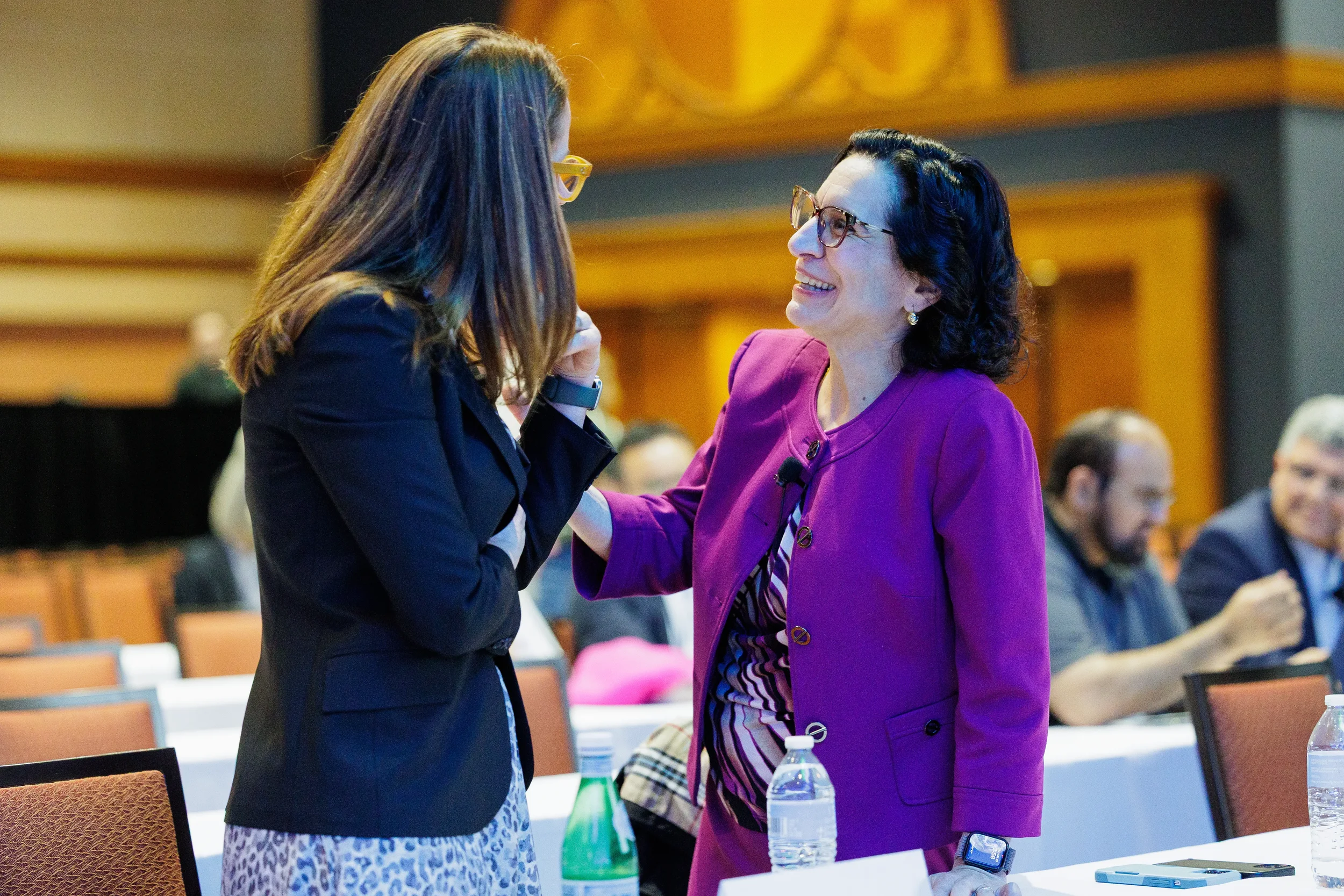 Two speakers share a warm greeting between seated tables in ballroom at Orlando corporate event