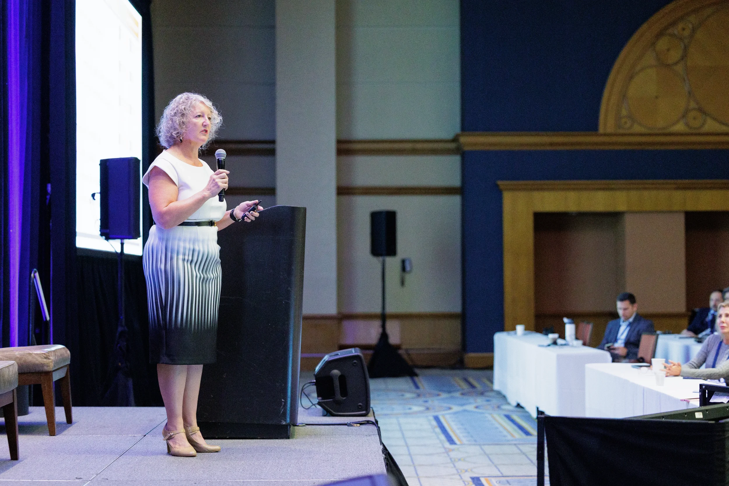Keynote speaker presents with microphone on stage in ornate Orlando conference ballroom