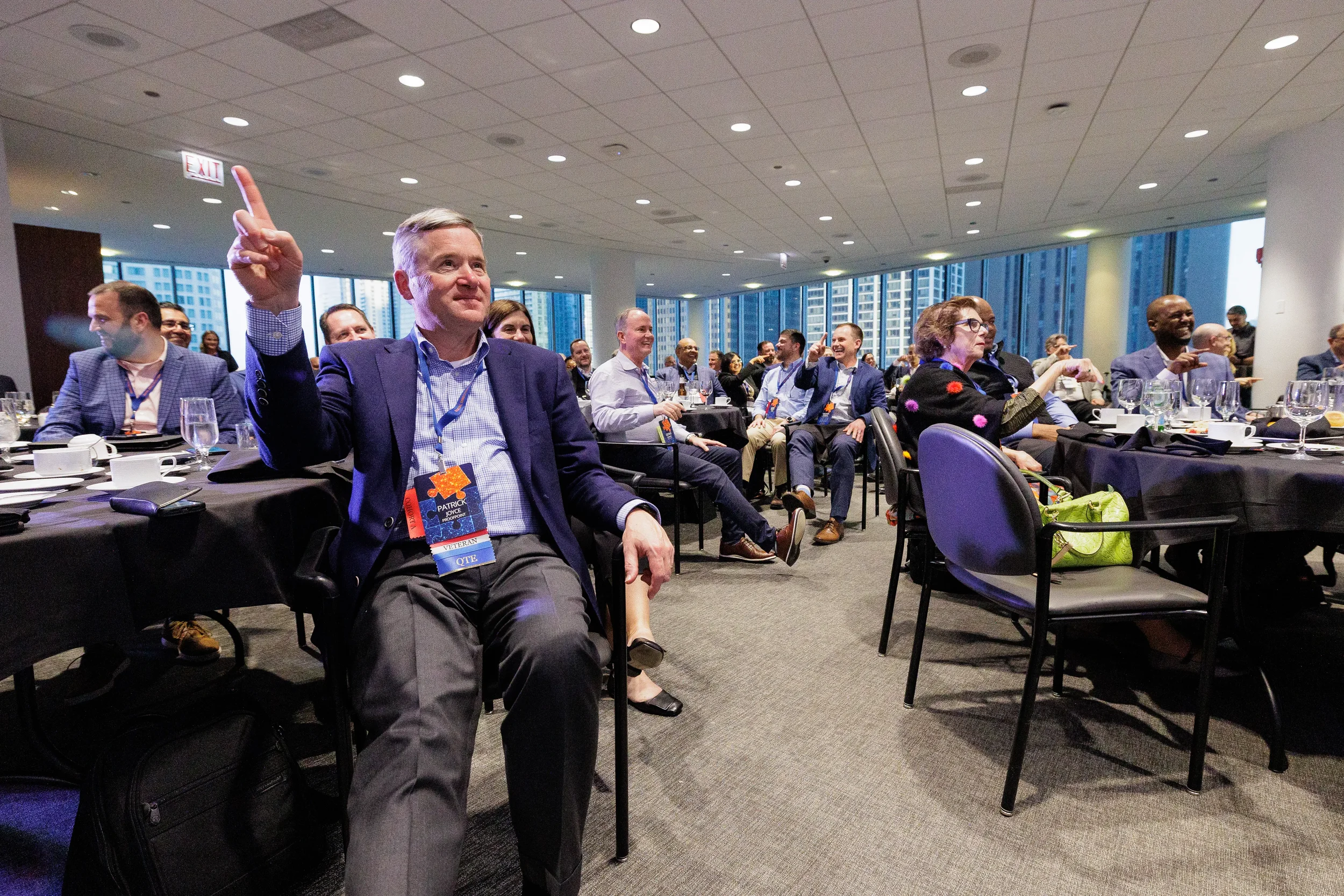 Attendee raises hand while seated at round table during Orlando corporate conference session with city views