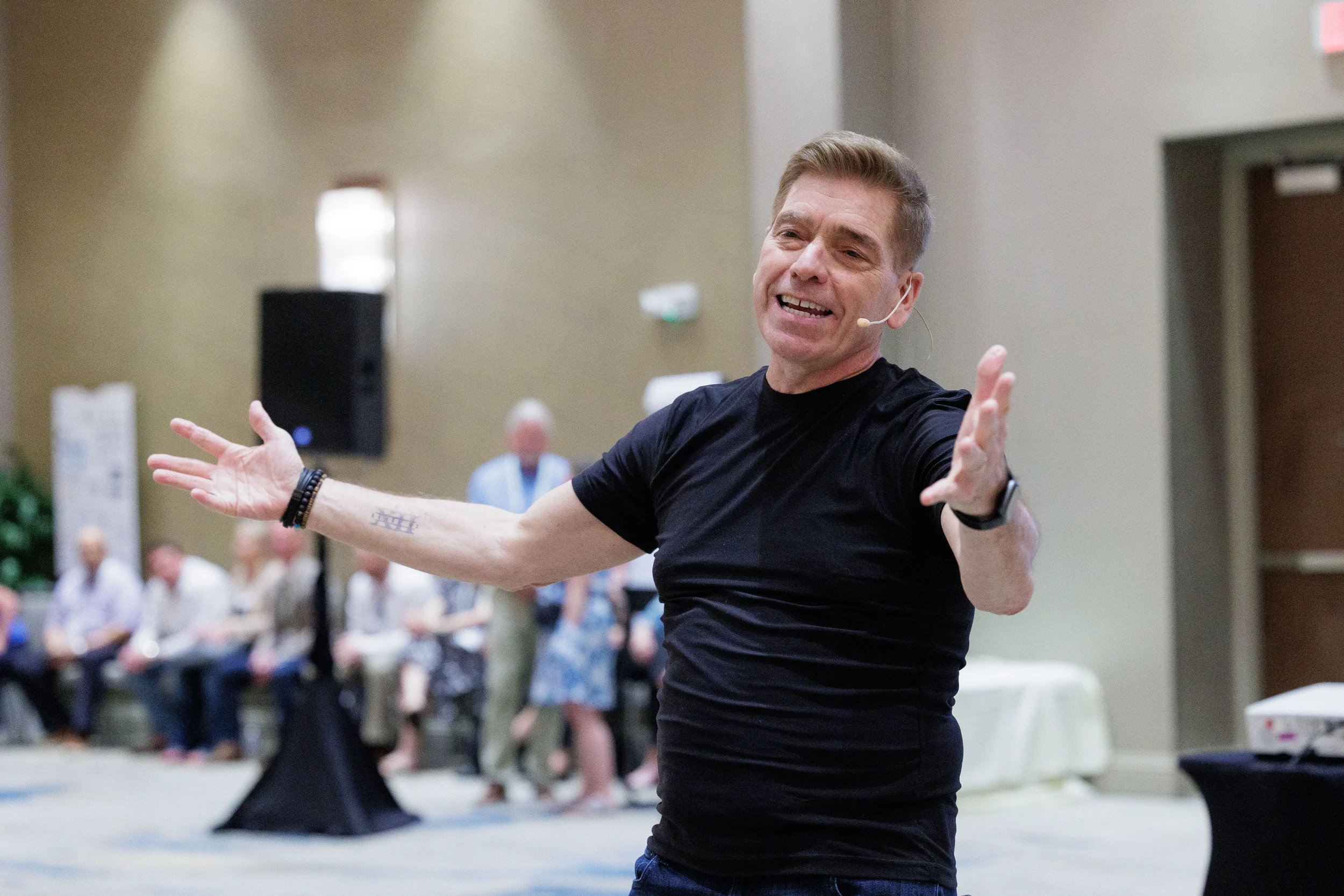 Energetic speaker with headset mic stretches arms wide addressing audience at Orlando corporate event