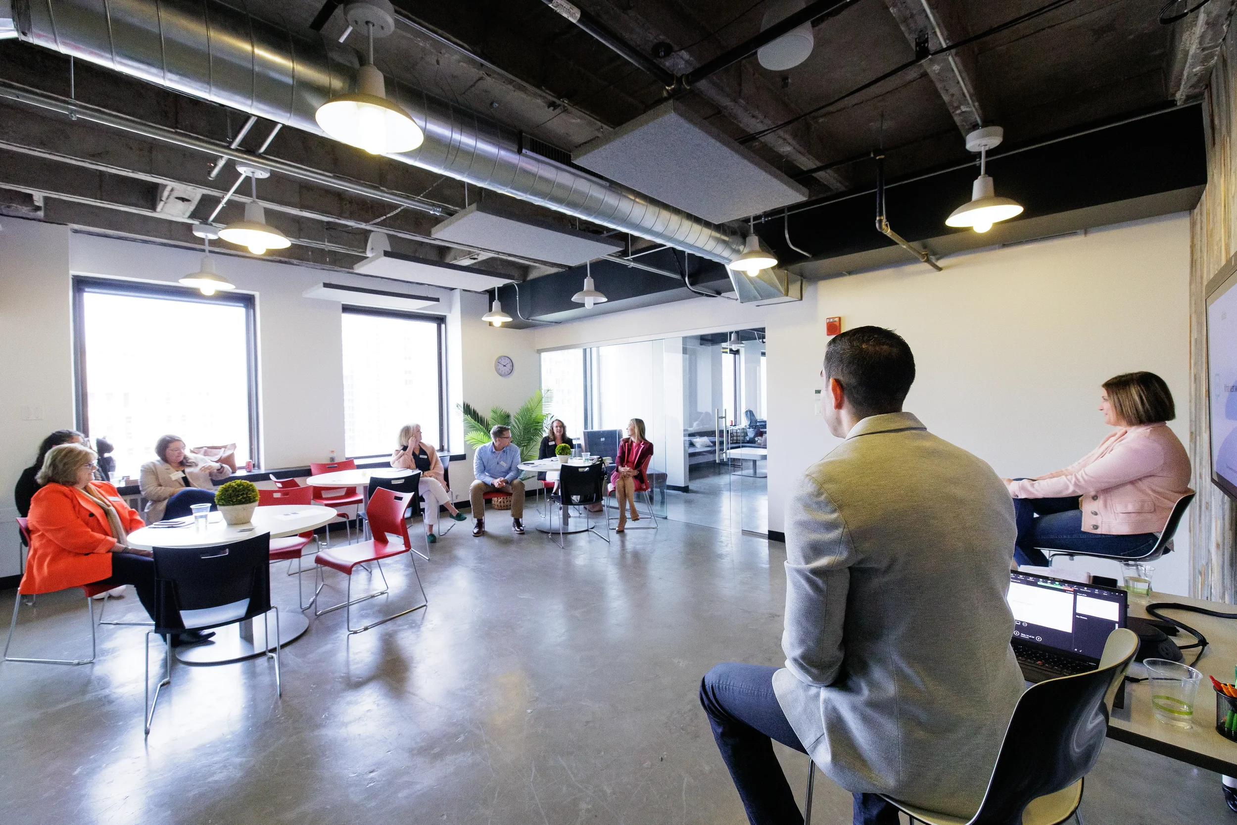 Man in gray jacket and woman in pink jacket present to a small group seated near bright windows in a modern office in Chicago