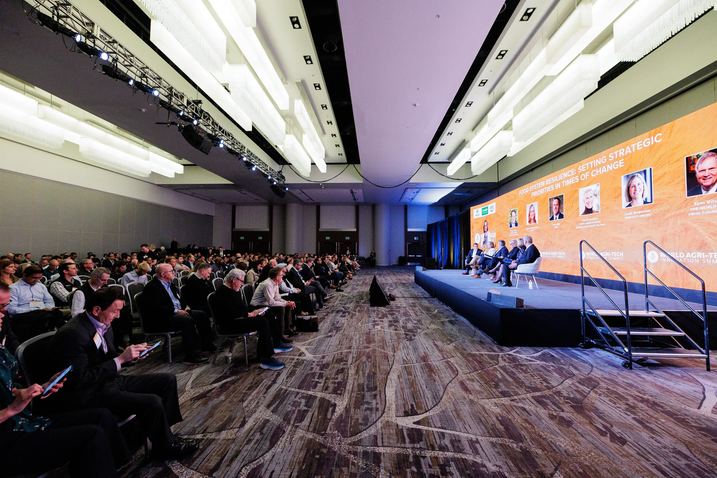 Full ballroom audience watches panel of speakers on branded stage with large screen at Orlando industry conference