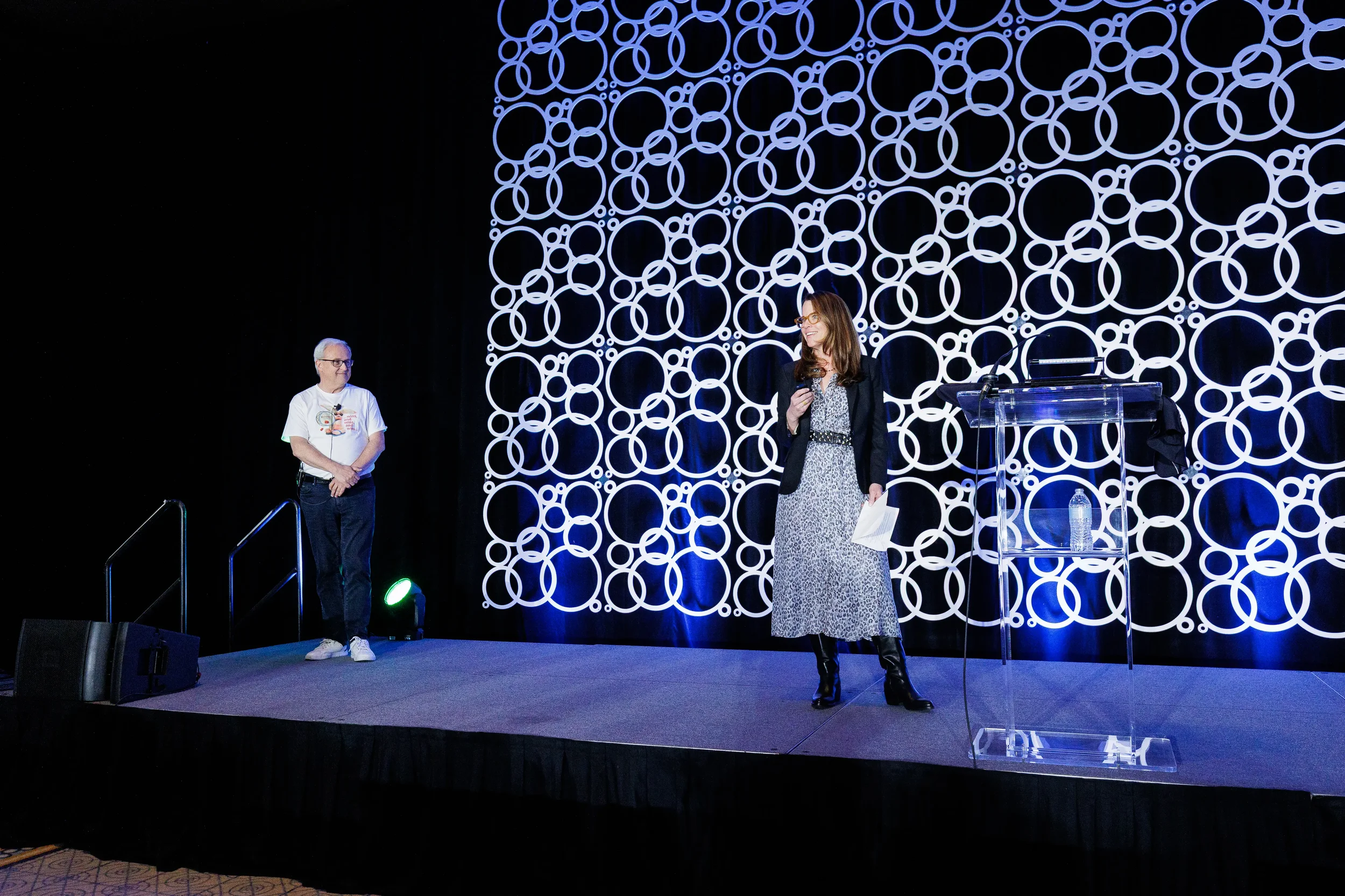 Two presenters share a moment on stage with circle-patterned backdrop at Orlando corporate conference