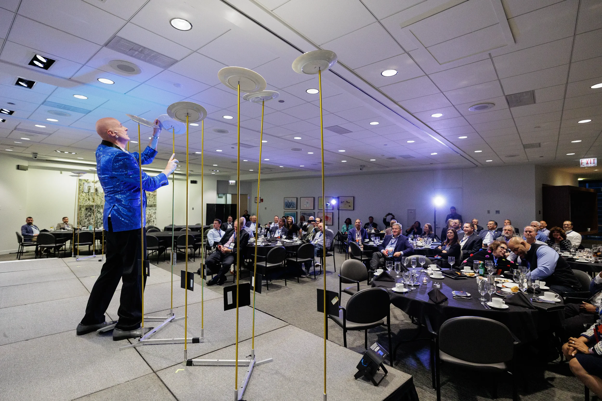 Entertainer in blue jacket spins plates on poles on stage before seated audience at Chicago corporate event