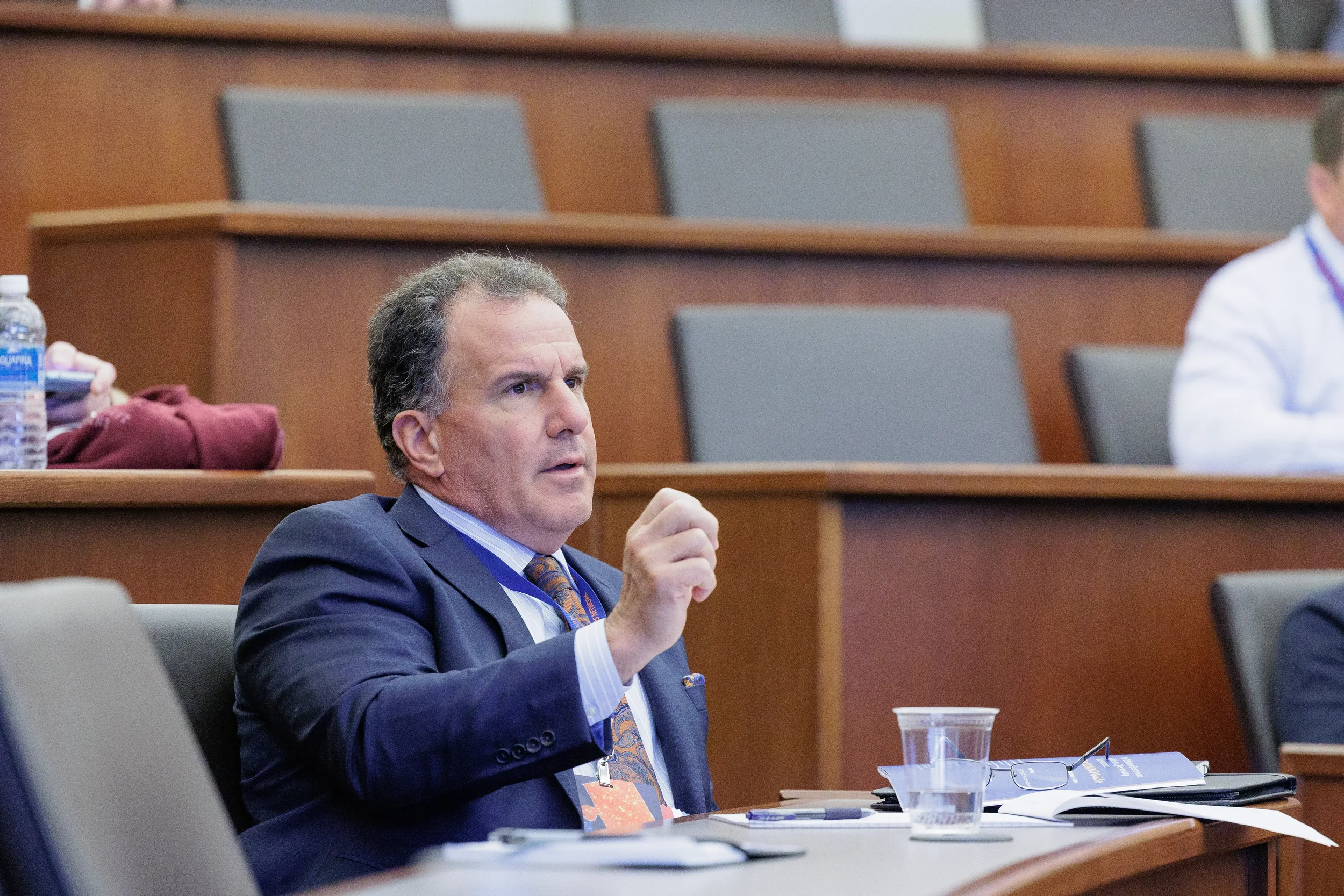 Suited attendee gestures while speaking from seat during Chicago industry conference session
