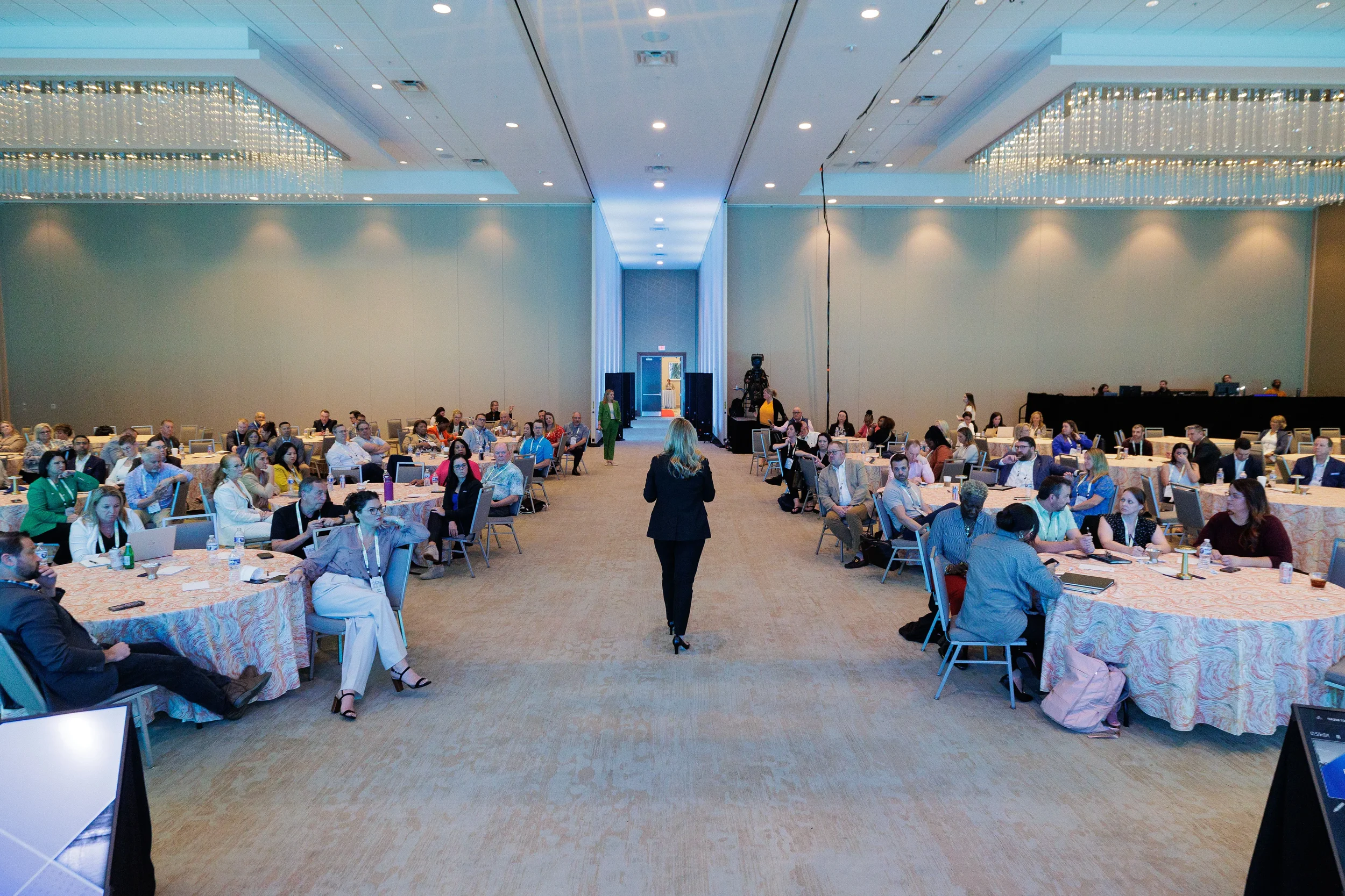 Female speaker walks center aisle of full ballroom audience at Orlando corporate conference session