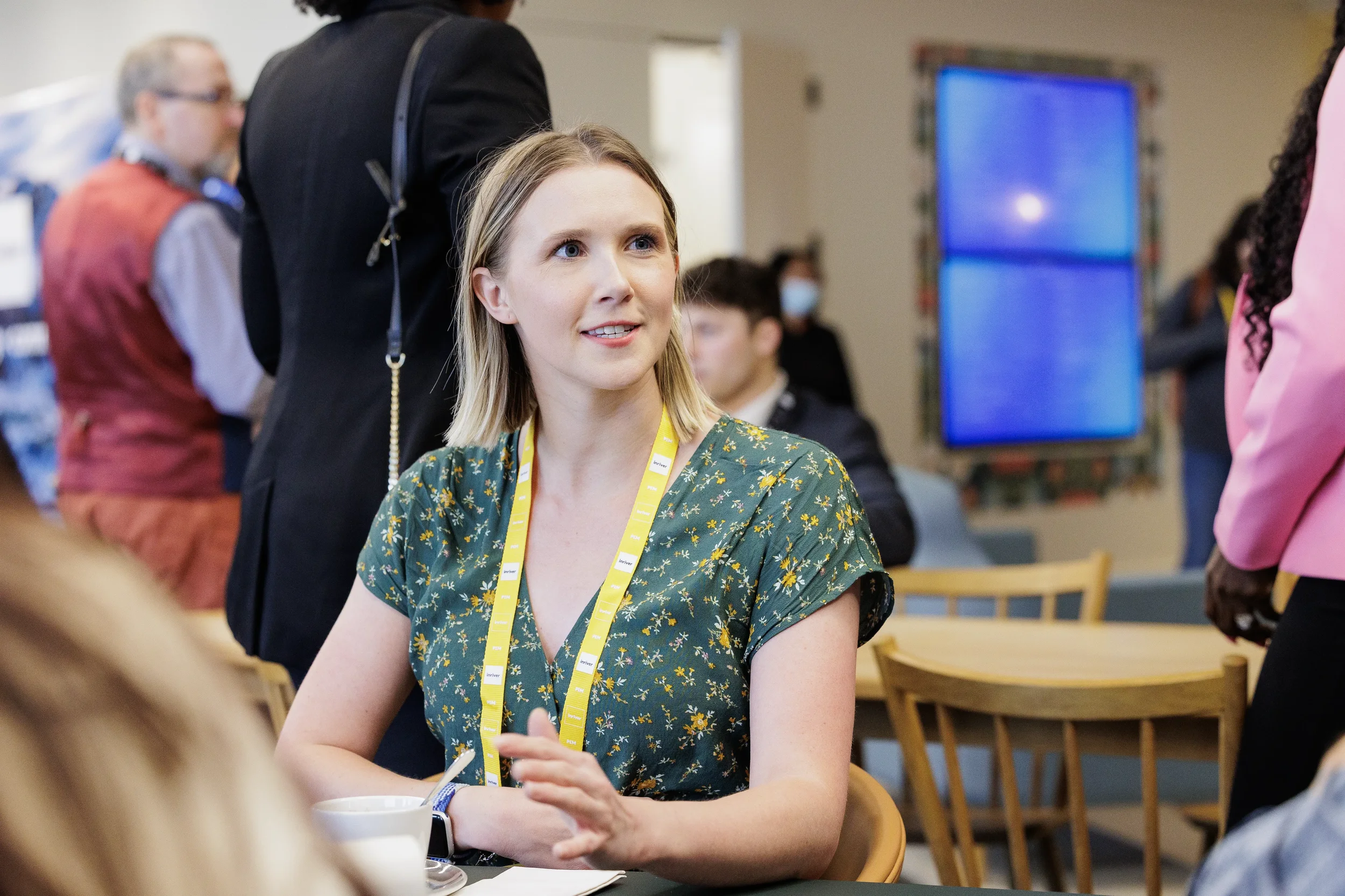 Attendee in floral top with yellow lanyard sits at table during Chicago corporate networking break