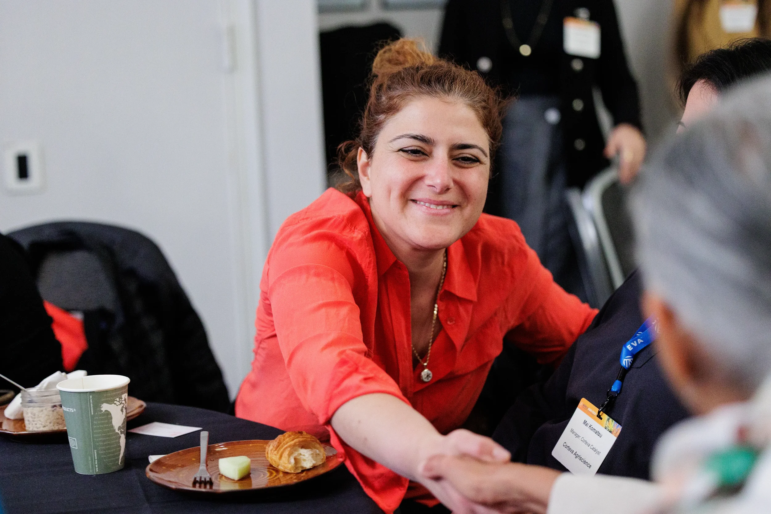 Attendee in red shirt smiles while shaking hands at seated networking session at Orlando industry conference