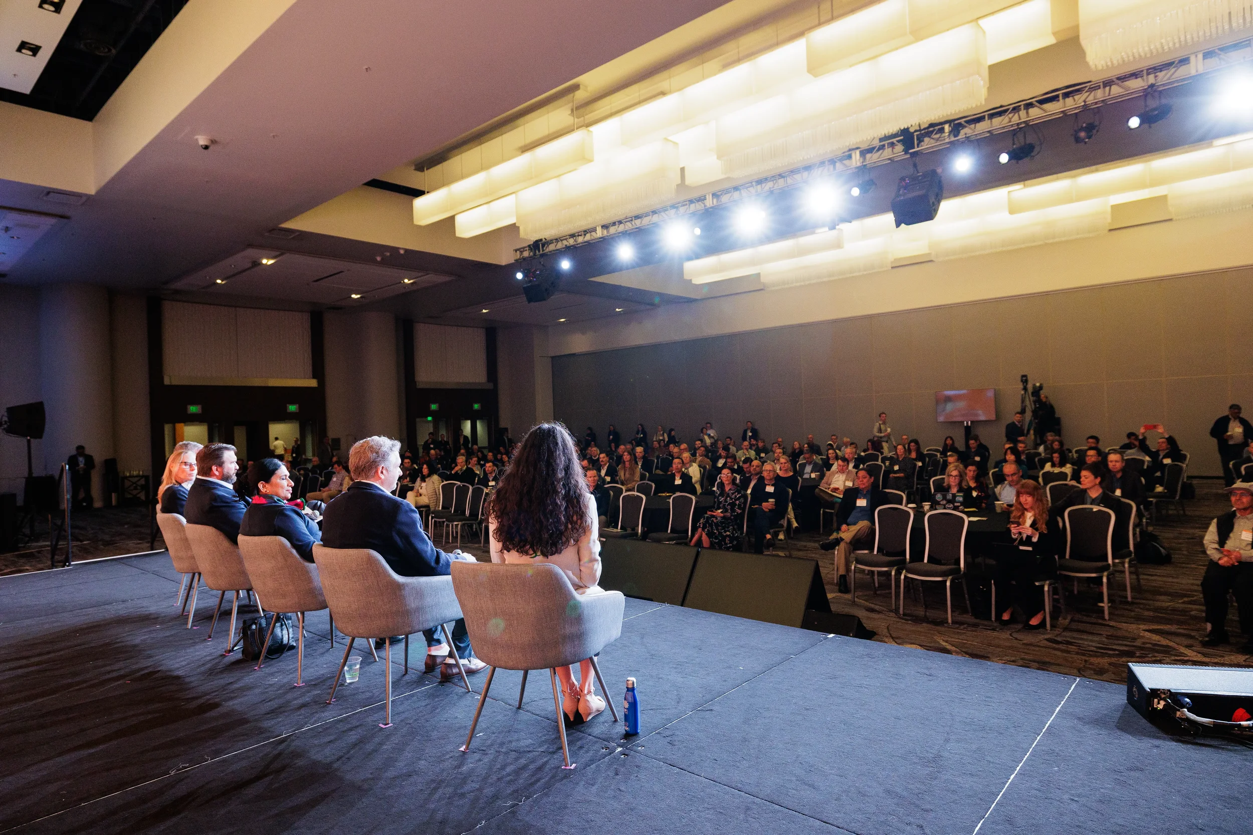 Five panelists seated on stage face a full audience during Chicago corporate event in hotel ballroom