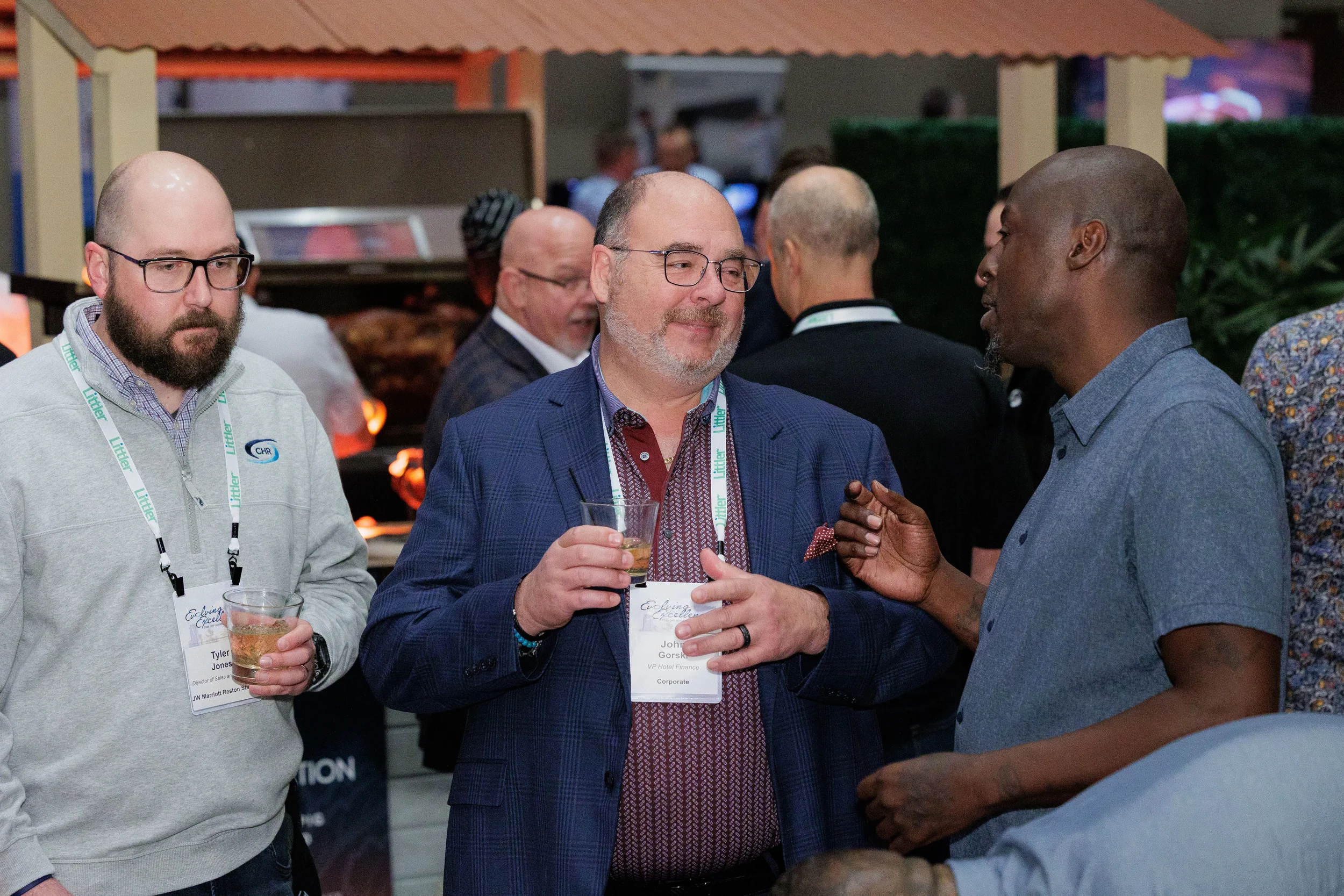 Three attendees with lanyards converse over drinks on expo floor at Chicago industry conference