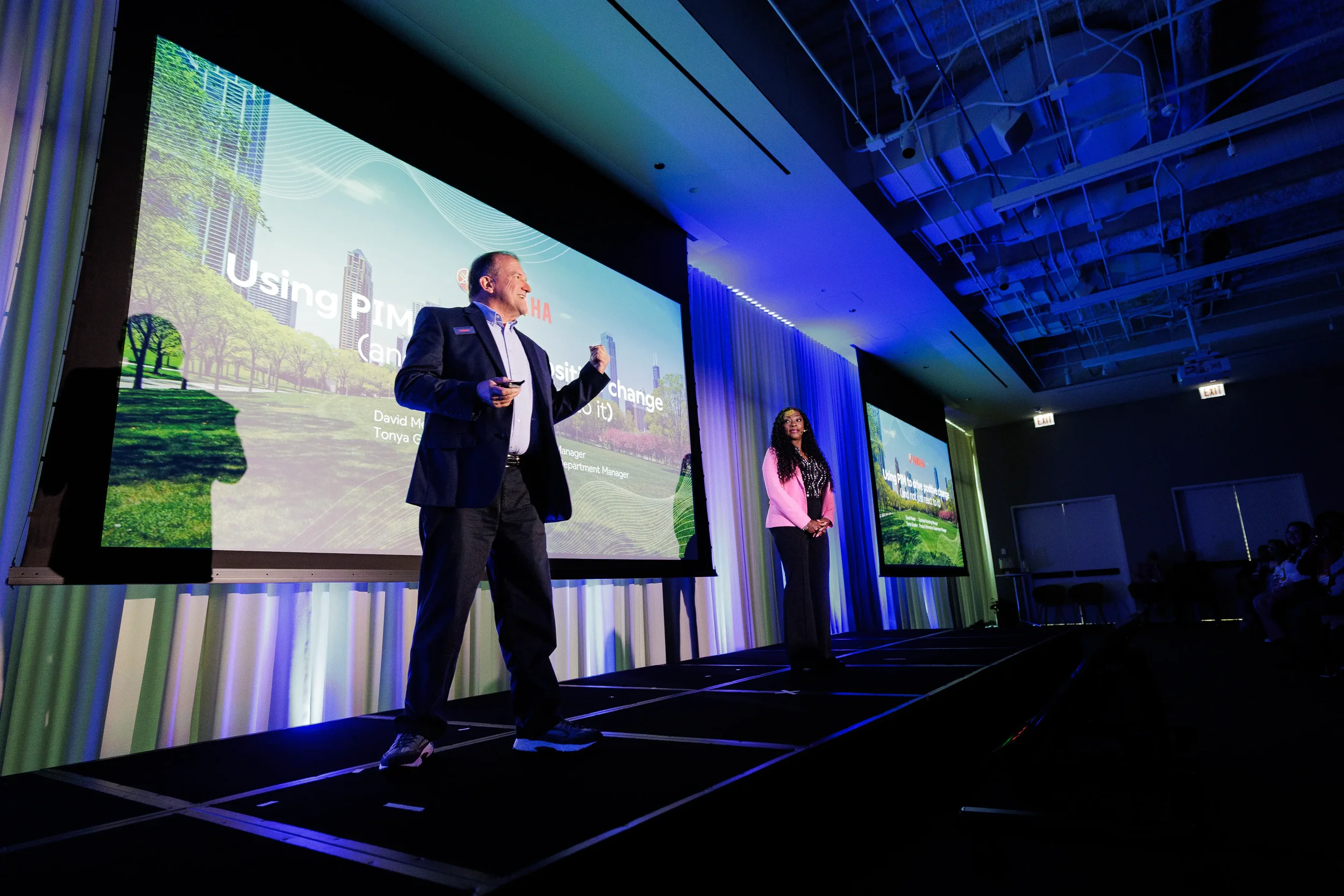 Two speakers present together on stage before green city skyline slide at Chicago corporate conference