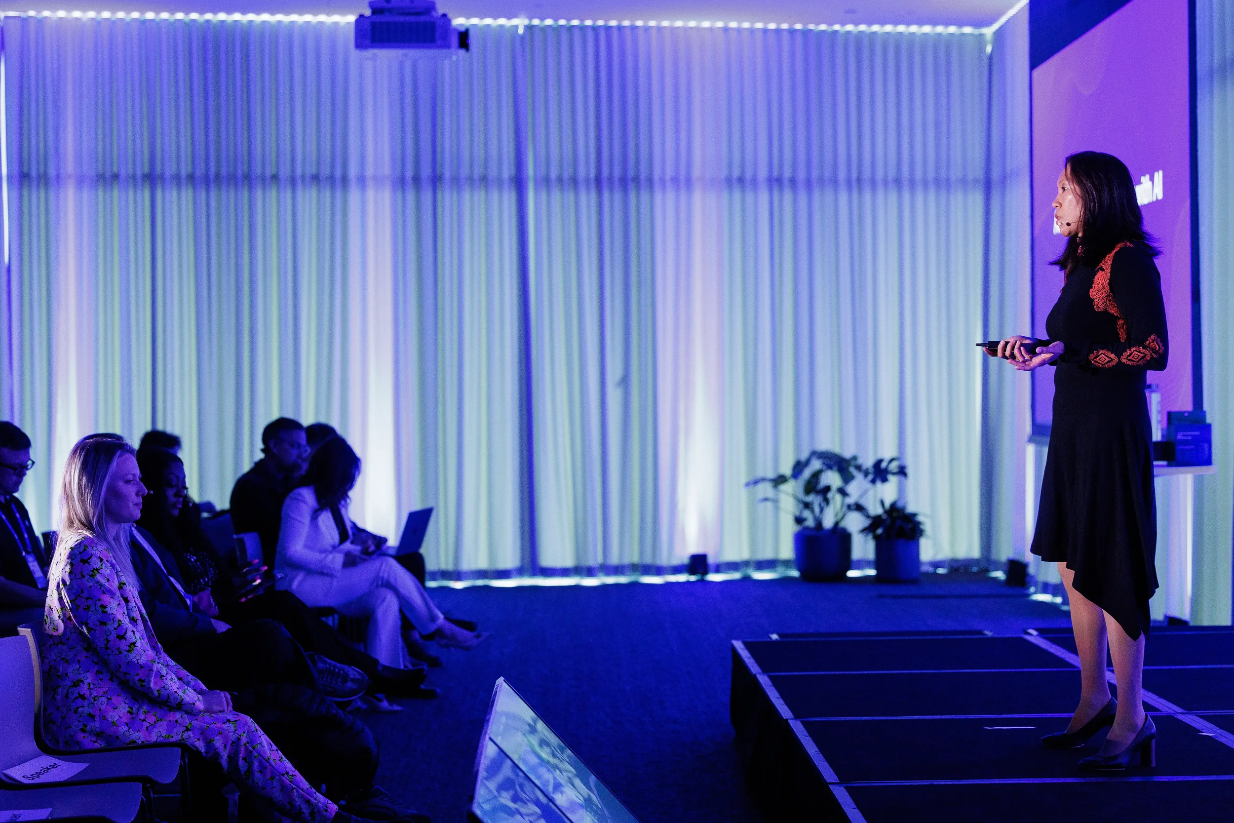 Speaker presents on stage to seated audience in purple-lit room at Chicago industry conference