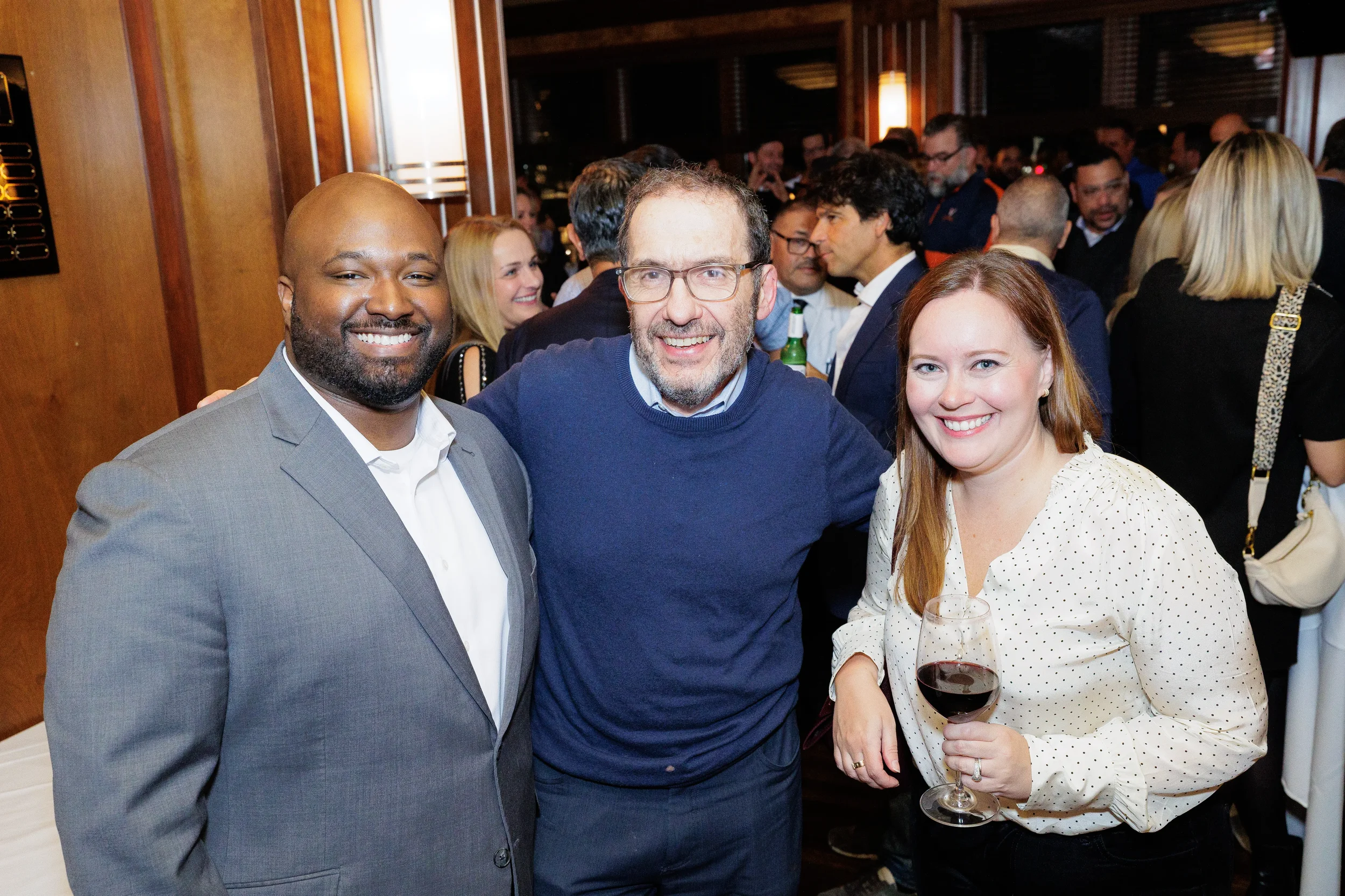 Three smiling adults pose for a photo at a crowded indoor event space in Orlando with wood-paneled walls