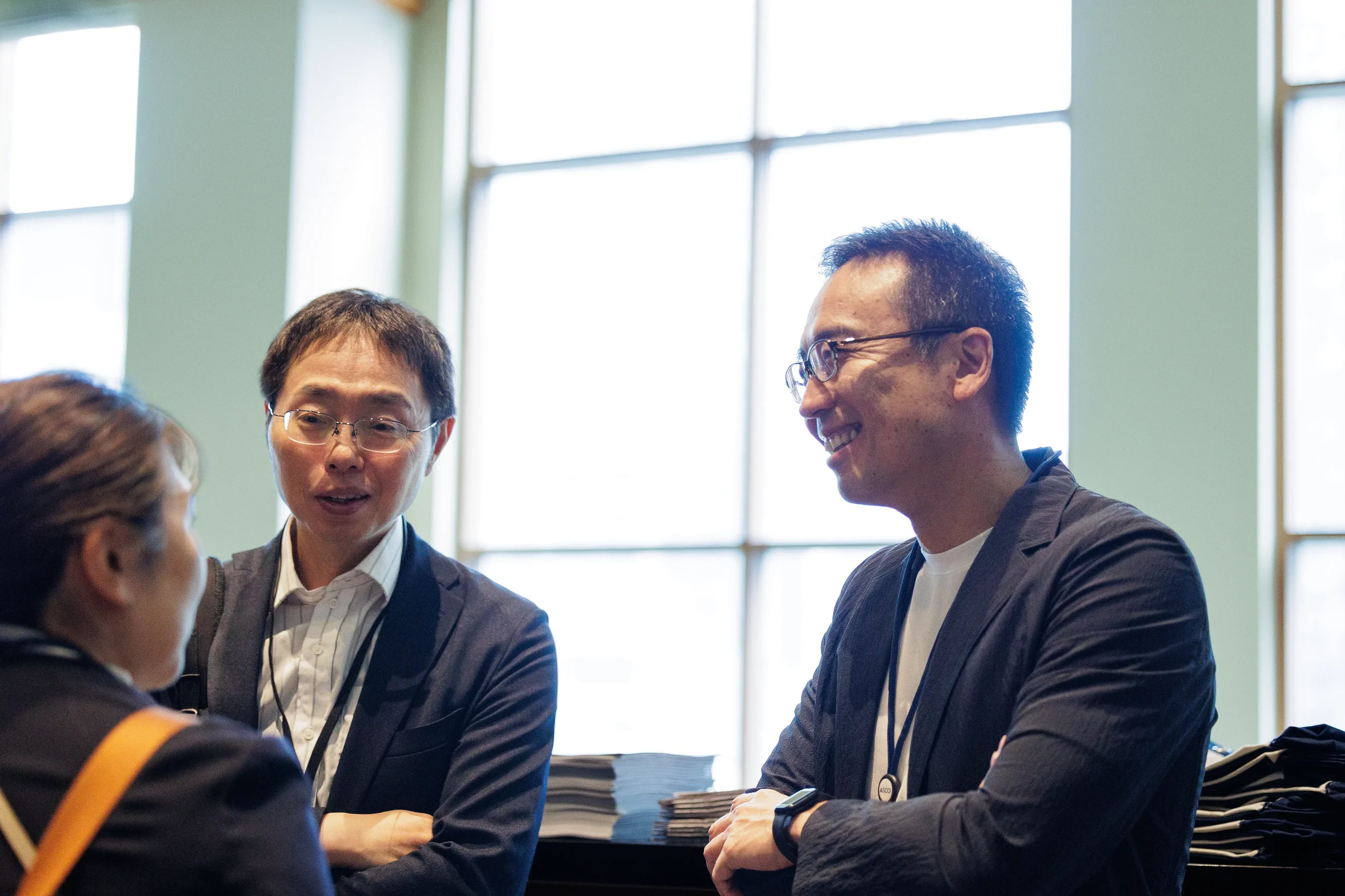 Two colleagues smile and talk by large windows at Chicago industry conference networking break