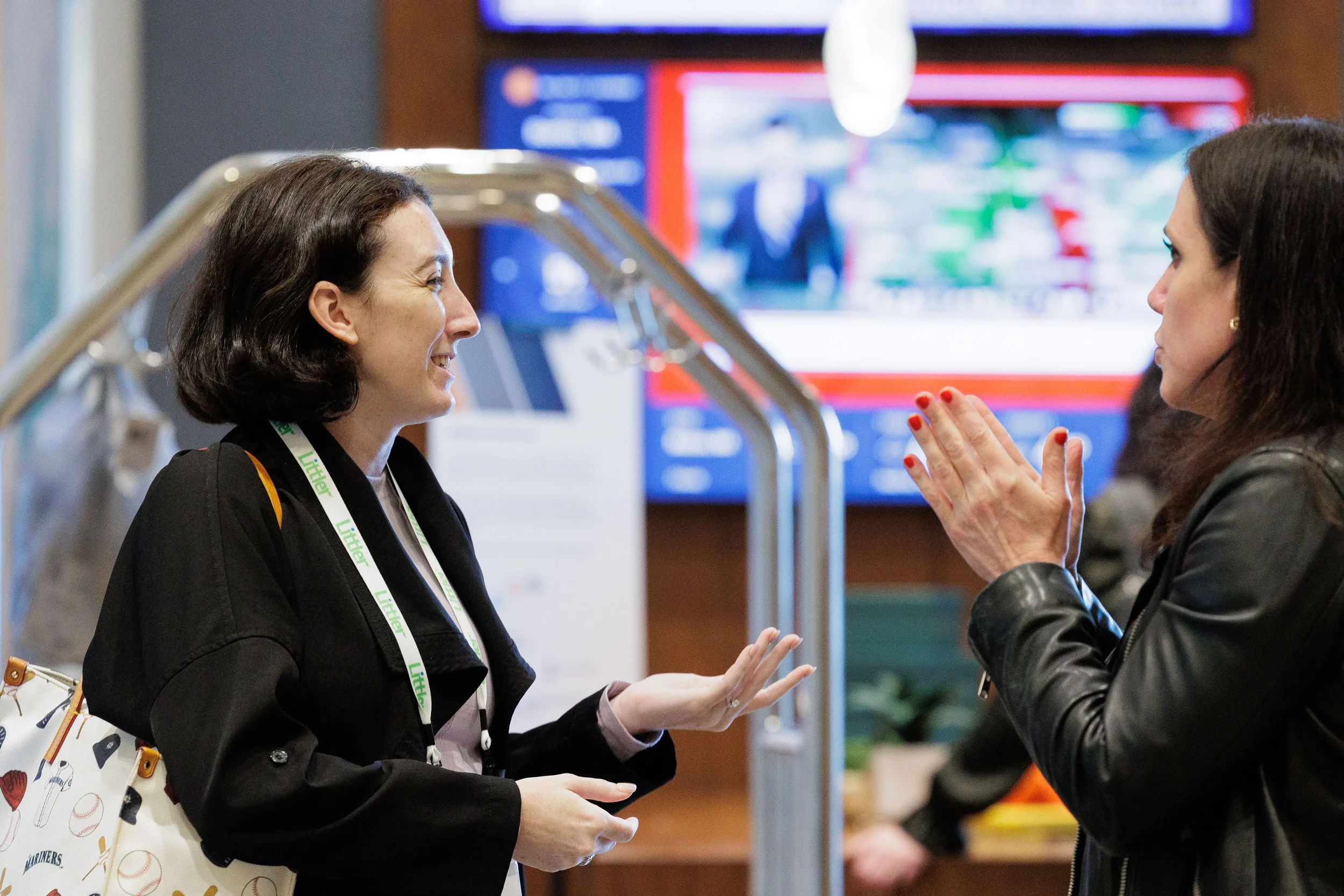 Two attendees with lanyards engage in animated conversation near digital displays at Orlando corporate conference