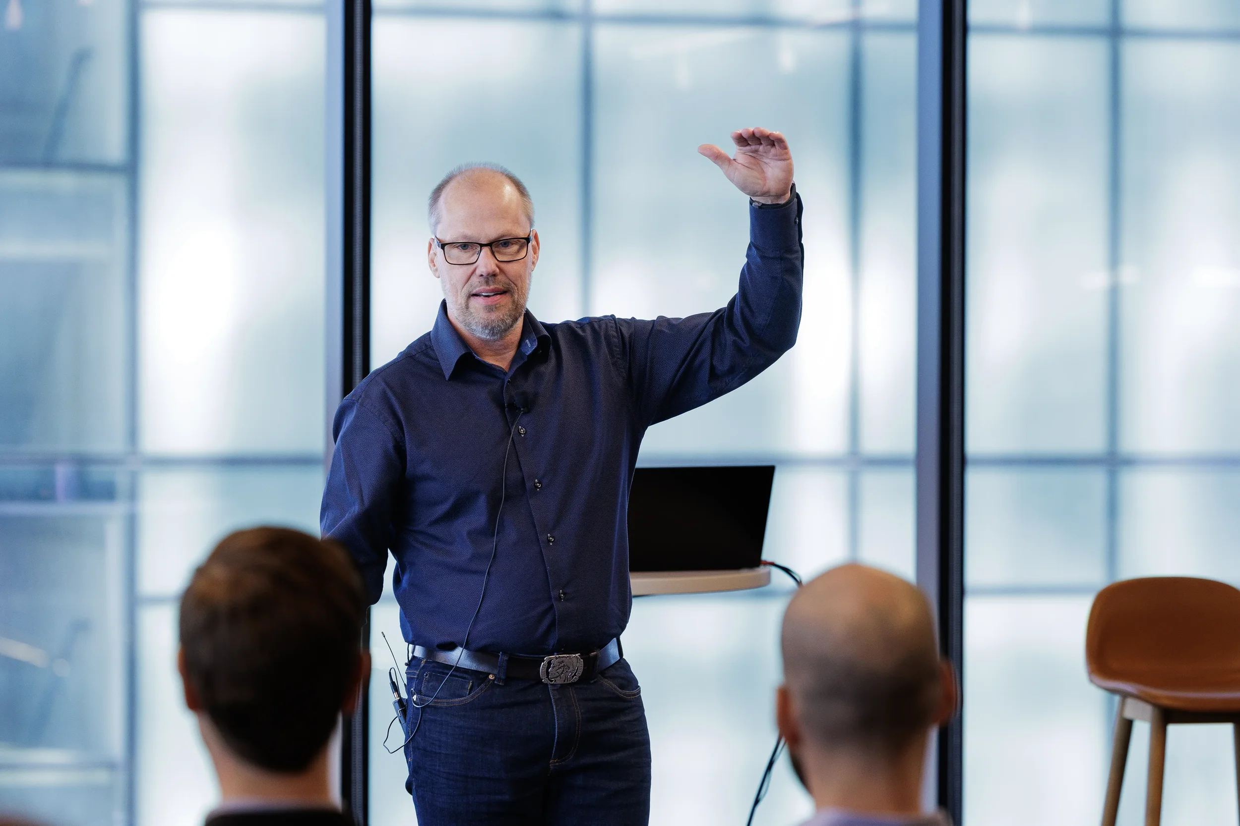 Speaker raises hand while presenting to audience in glass-walled room at Orlando industry conference