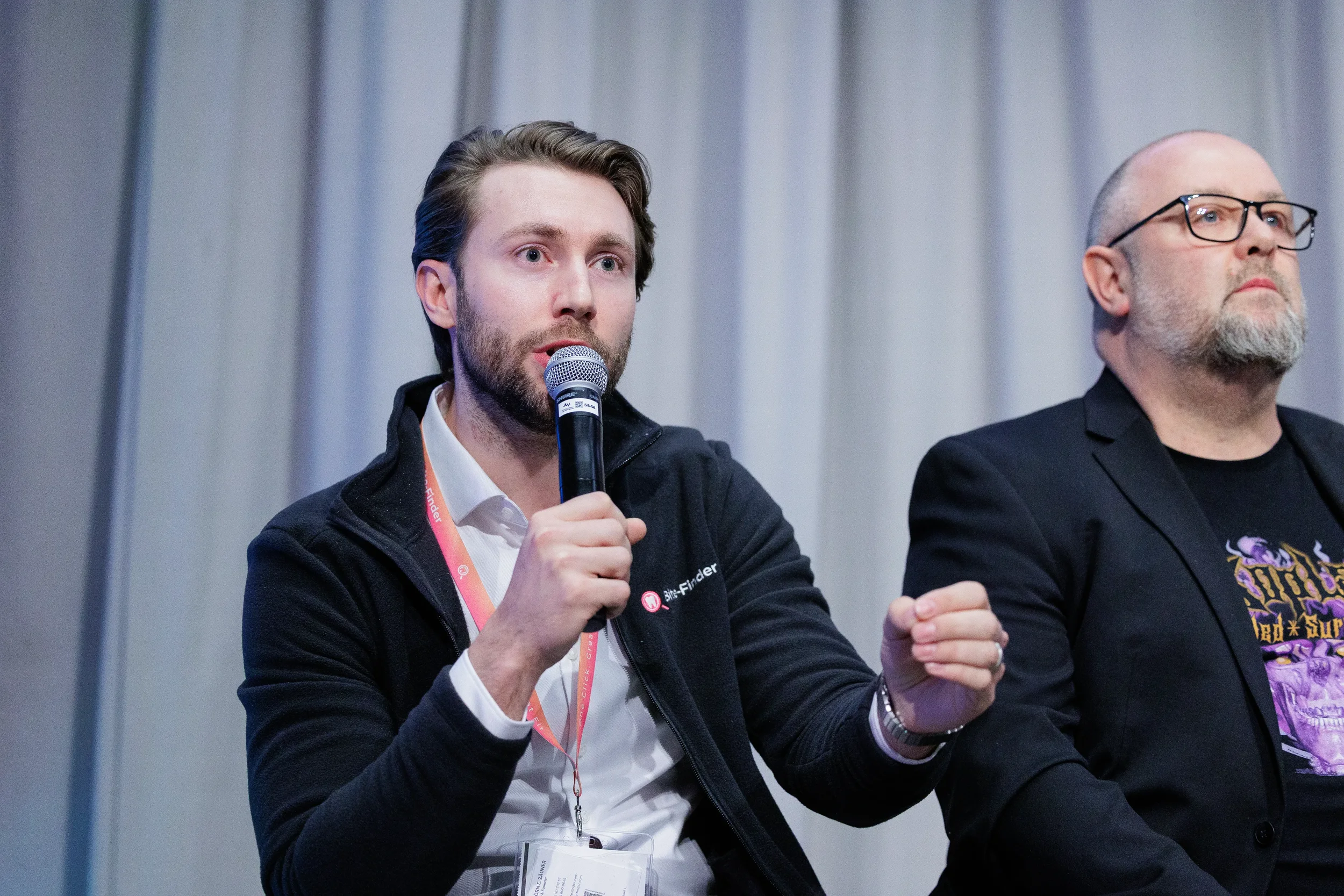 Lanyard-wearing panelist speaks into microphone while gesturing during Orlando industry conference panel