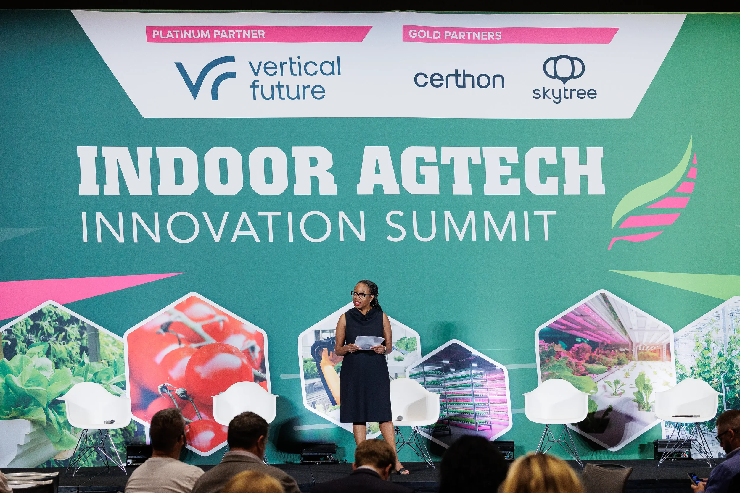Keynote speaker stands center stage in front of large branded backdrop addressing audience at Orlando industry conference