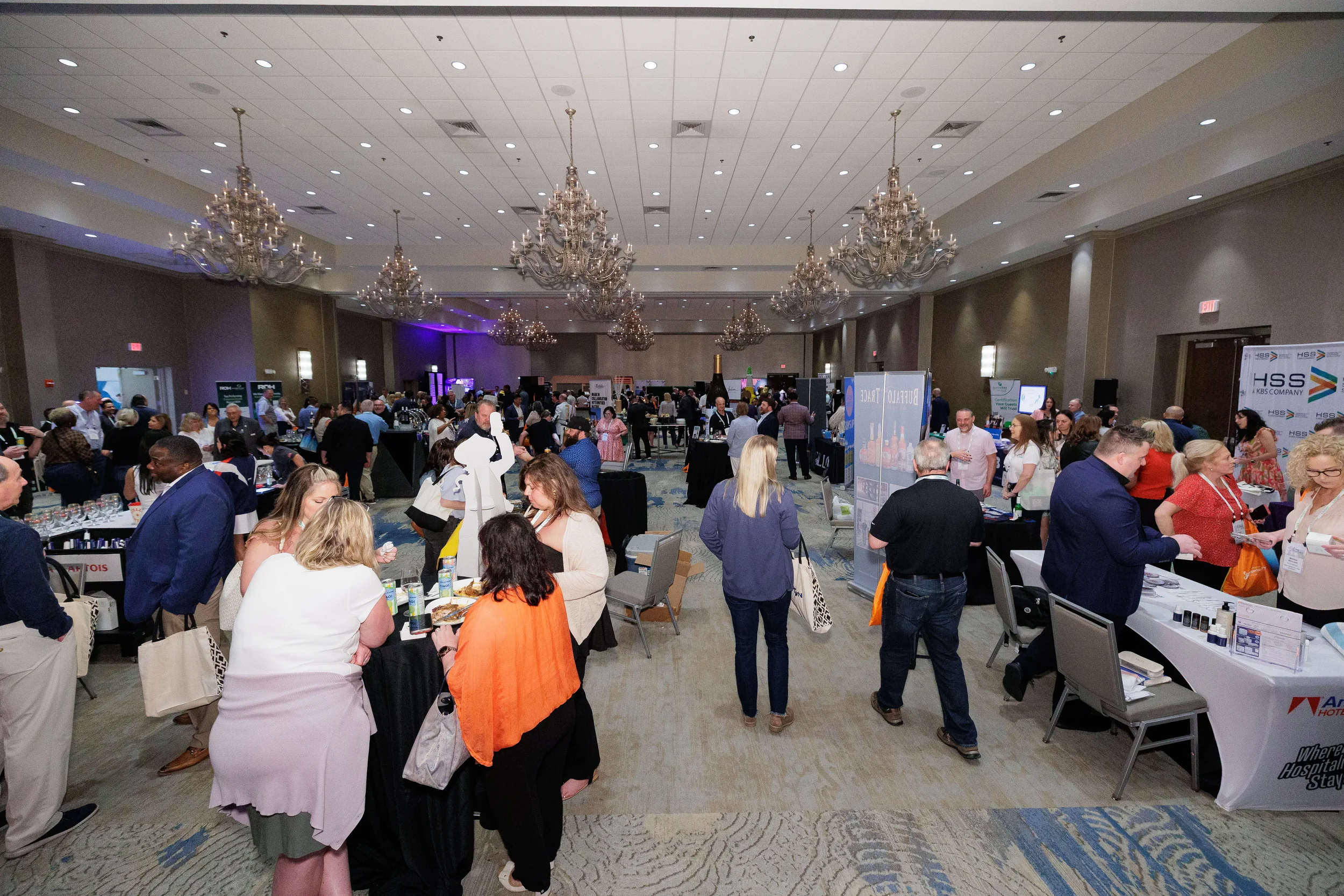 Attendees browse exhibitor booths on trade show floor in chandelier ballroom at Orlando corporate conference