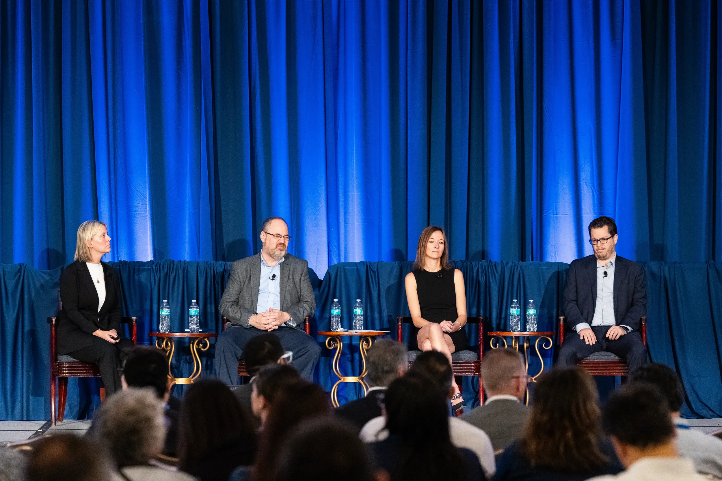 Four panelists seated on stage during panel discussion at Orlando conference in ornate ballroom