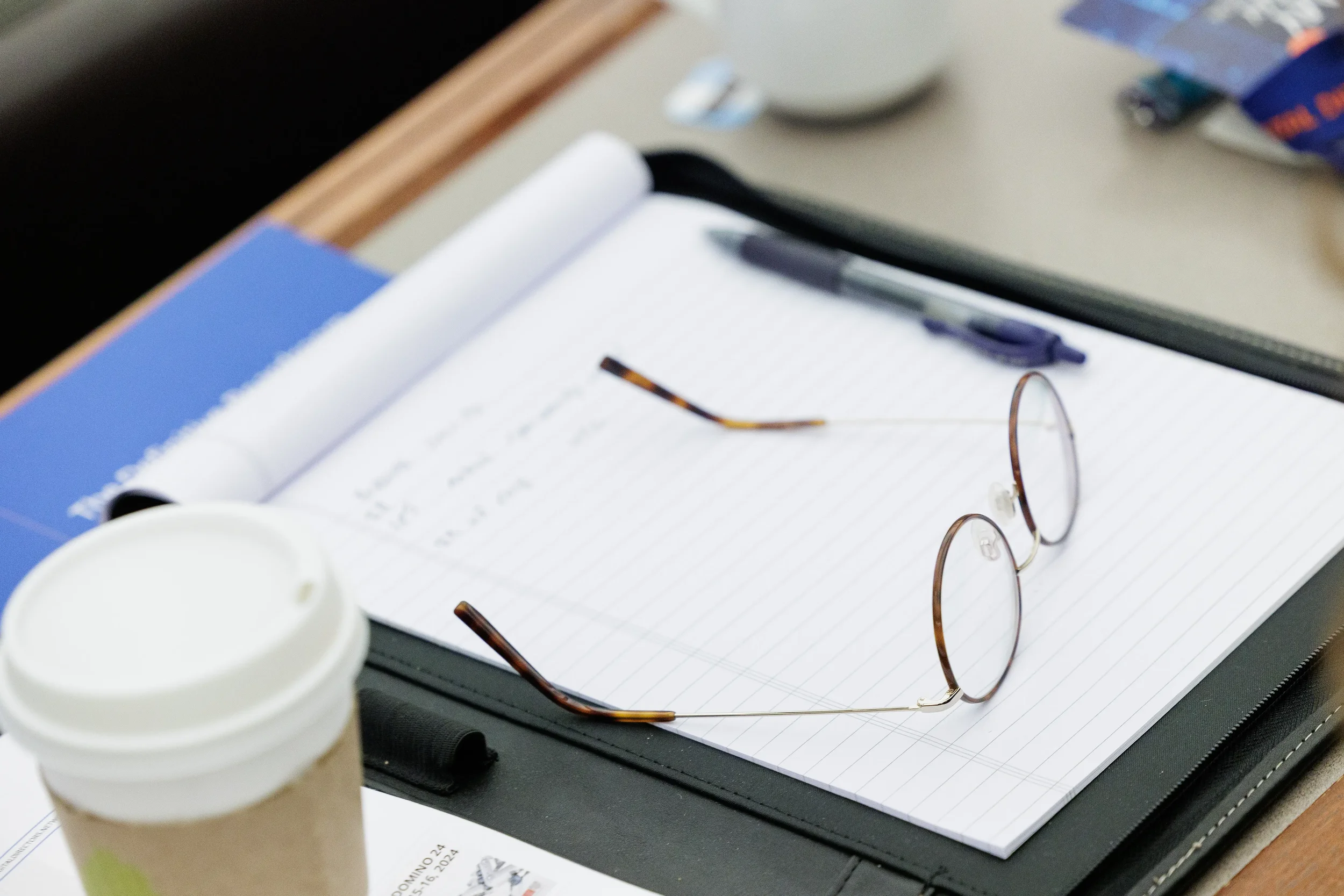 Glasses, notebook, pen and coffee cup on attendee desk during Chicago industry conference session