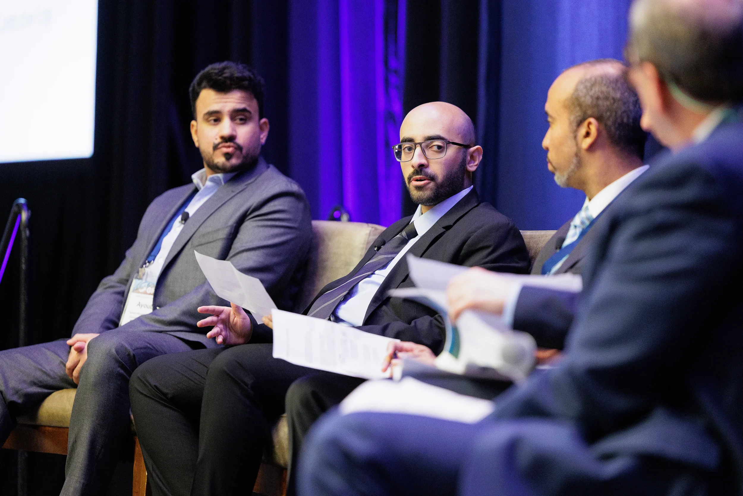 Three professionals in suits sit on a stage during a panel discussion in Chicago with a vibrant purple backdrop