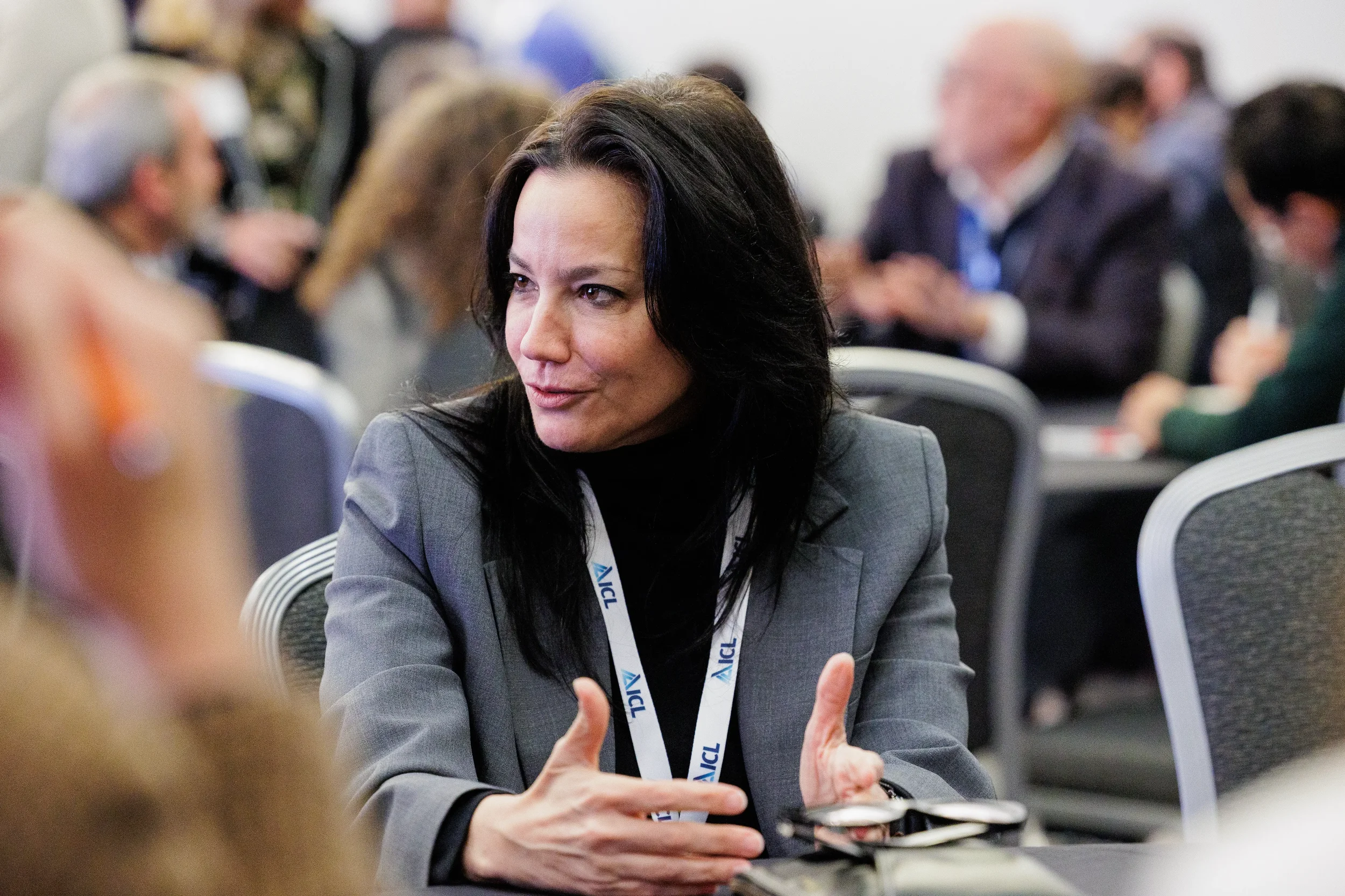 Attendee with lanyard gestures with hands while speaking during seated networking session at Orlando conference