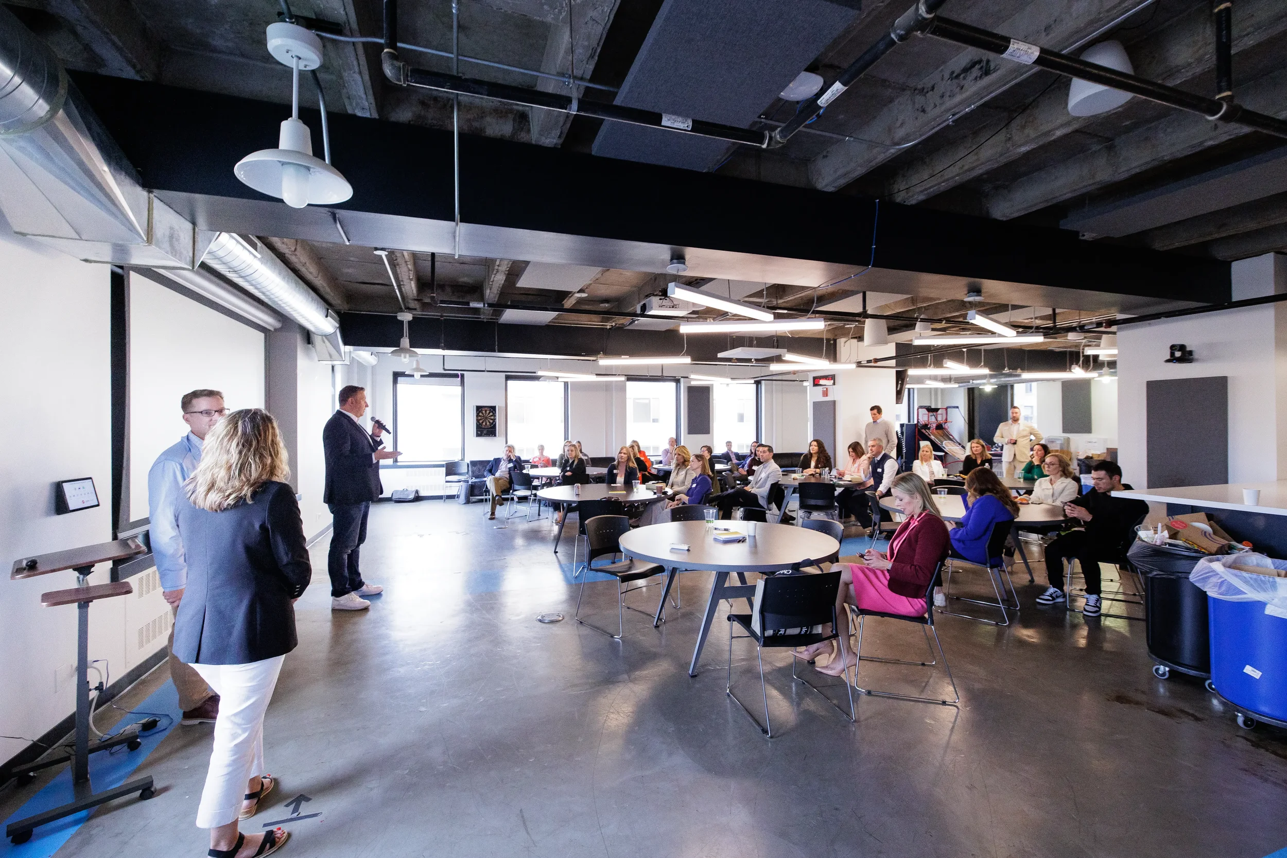 Wide view of full conference room with speaker at front and attendees seated at round tables in Chicago