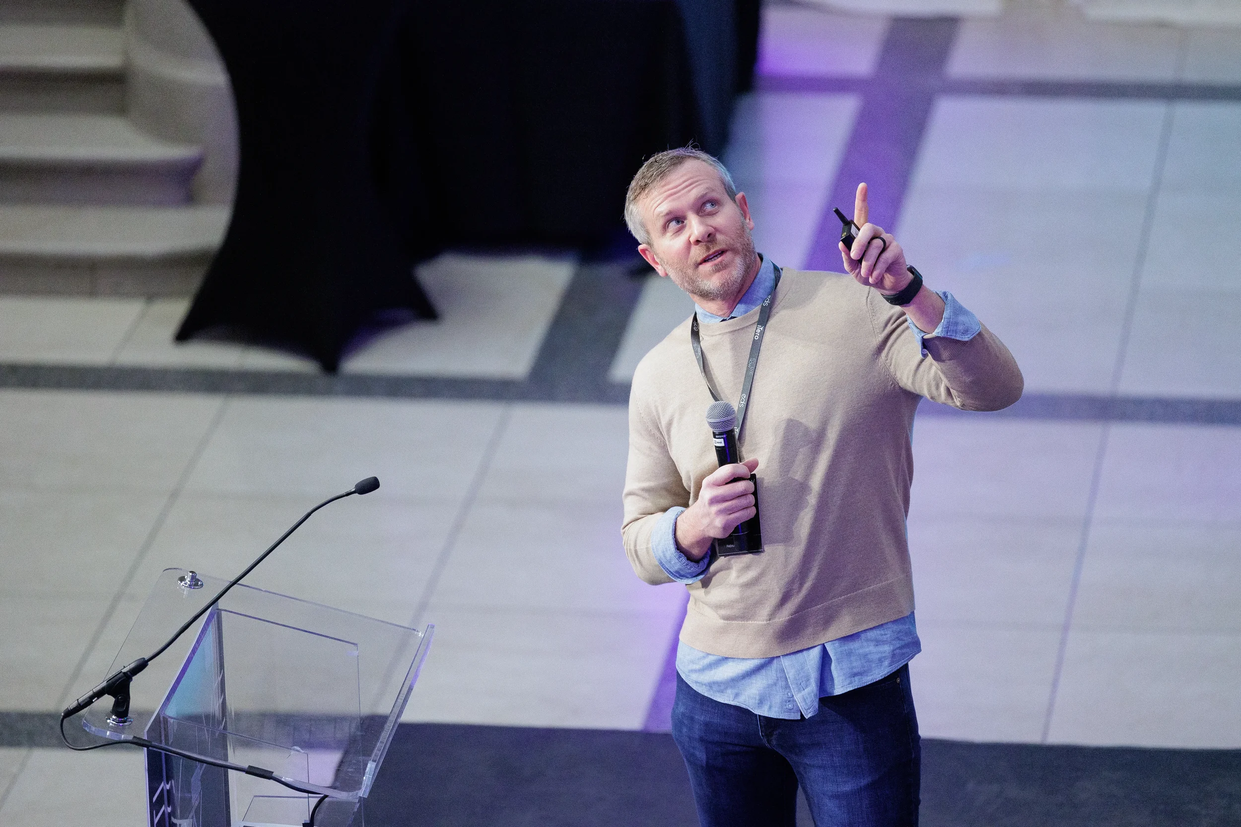 Speaker holds microphone and points upward while presenting on stage at Orlando corporate event