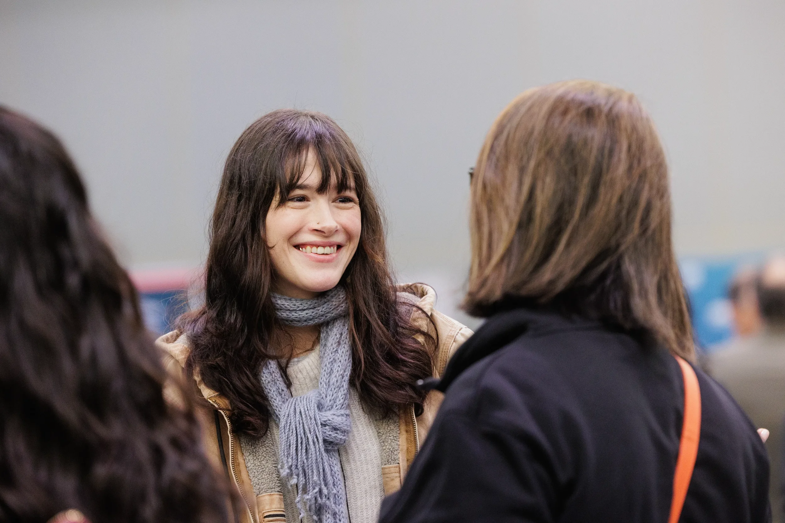 Smiling badged attendee in gray scarf converses with others during networking at Chicago corporate conference