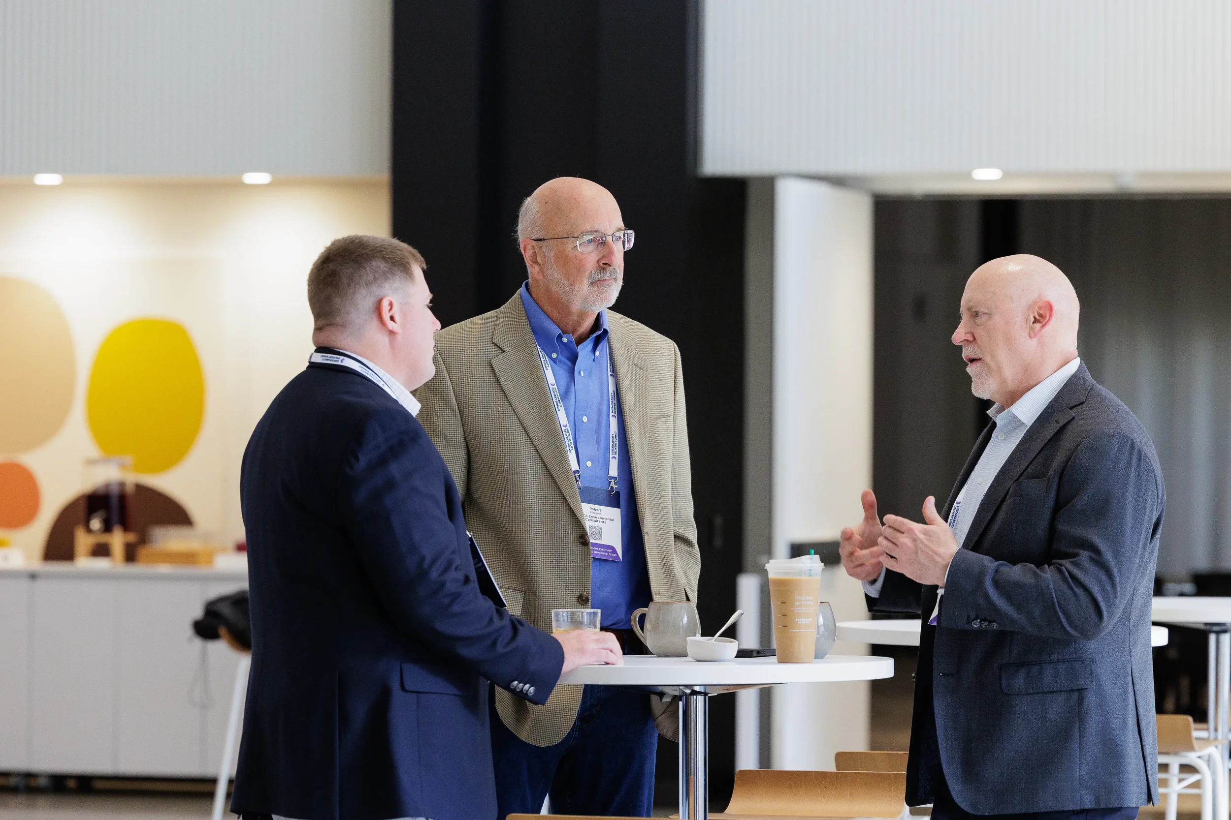 Three attendees converse at standing table over coffee during Orlando corporate conference