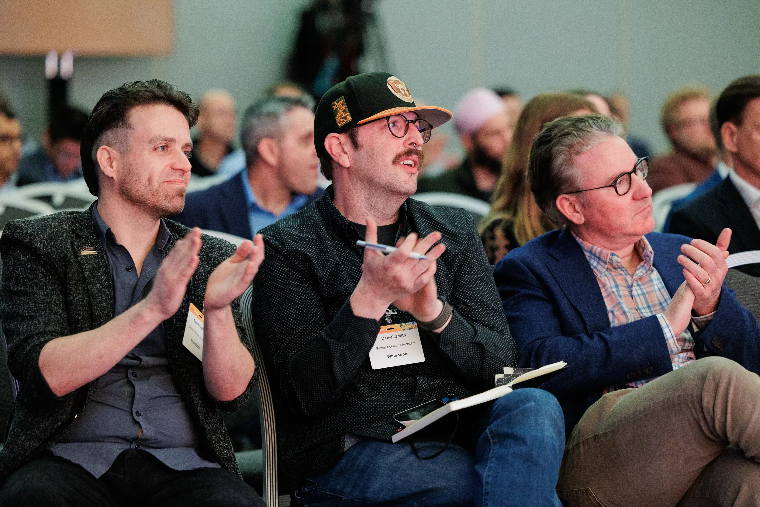 Three attendees with name badges applaud during seated session at Chicago industry conference
