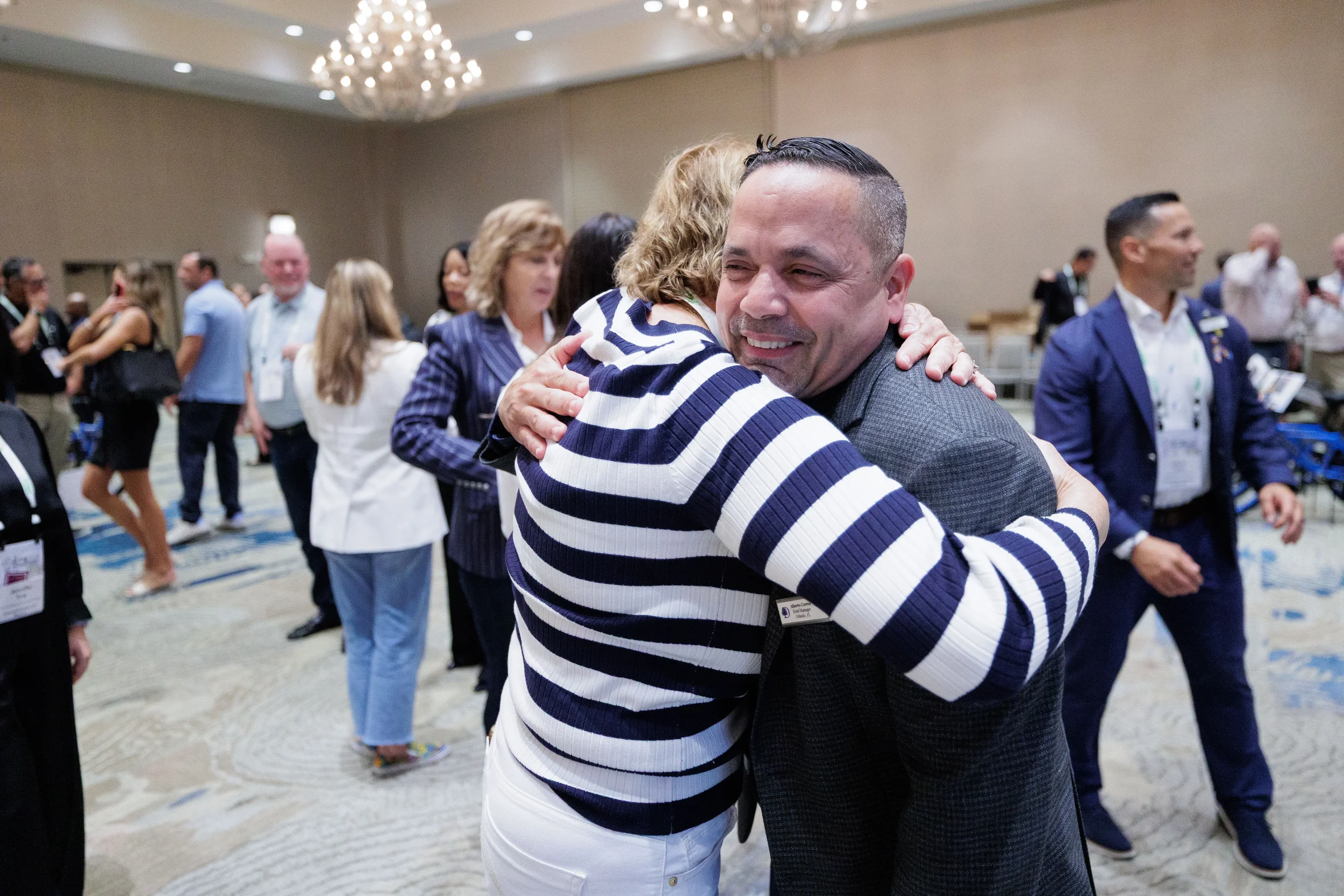 Two attendees embrace warmly during networking in chandelier ballroom at Orlando corporate event
