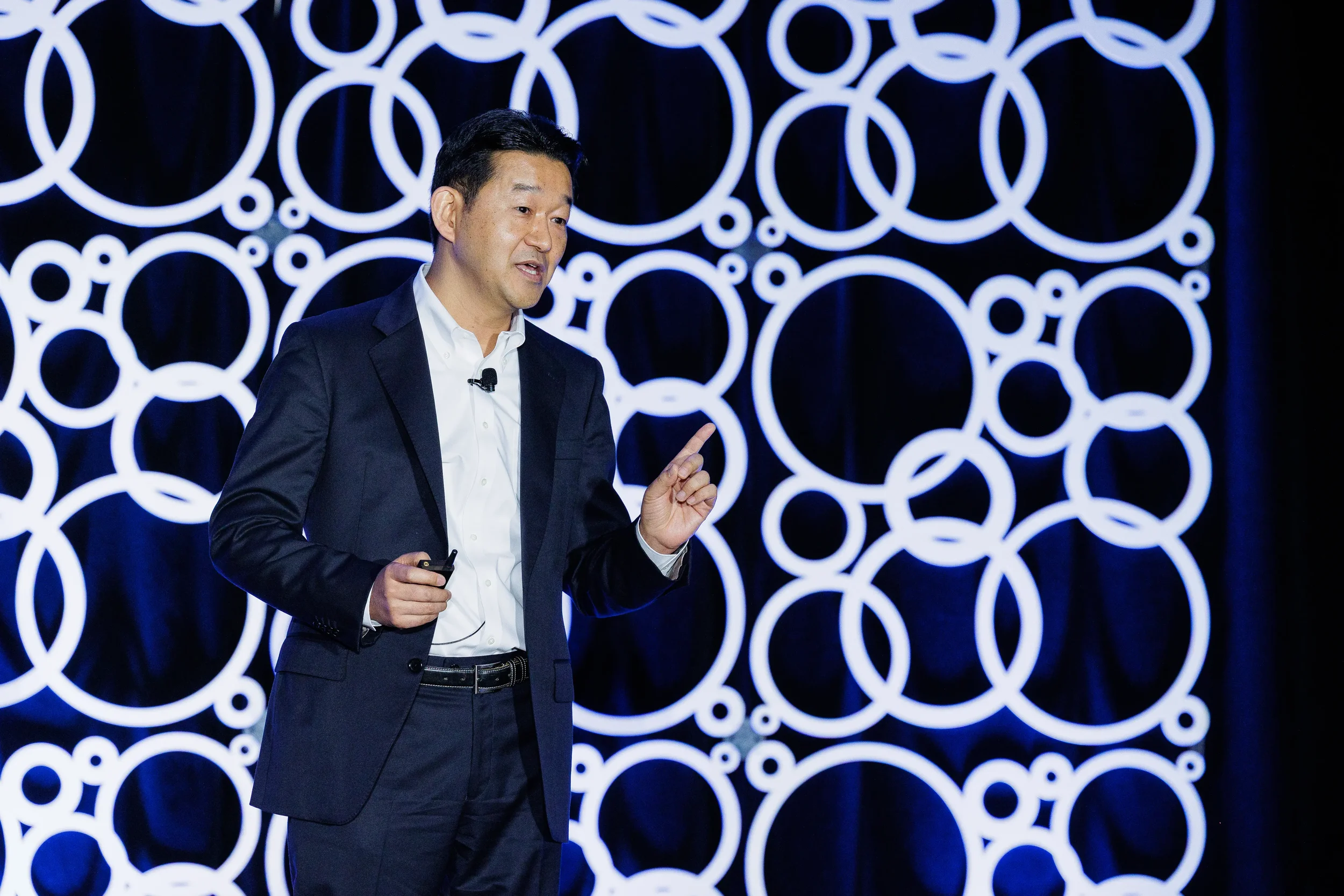 Speaker points while presenting on stage with circular backdrop at Orlando industry conference