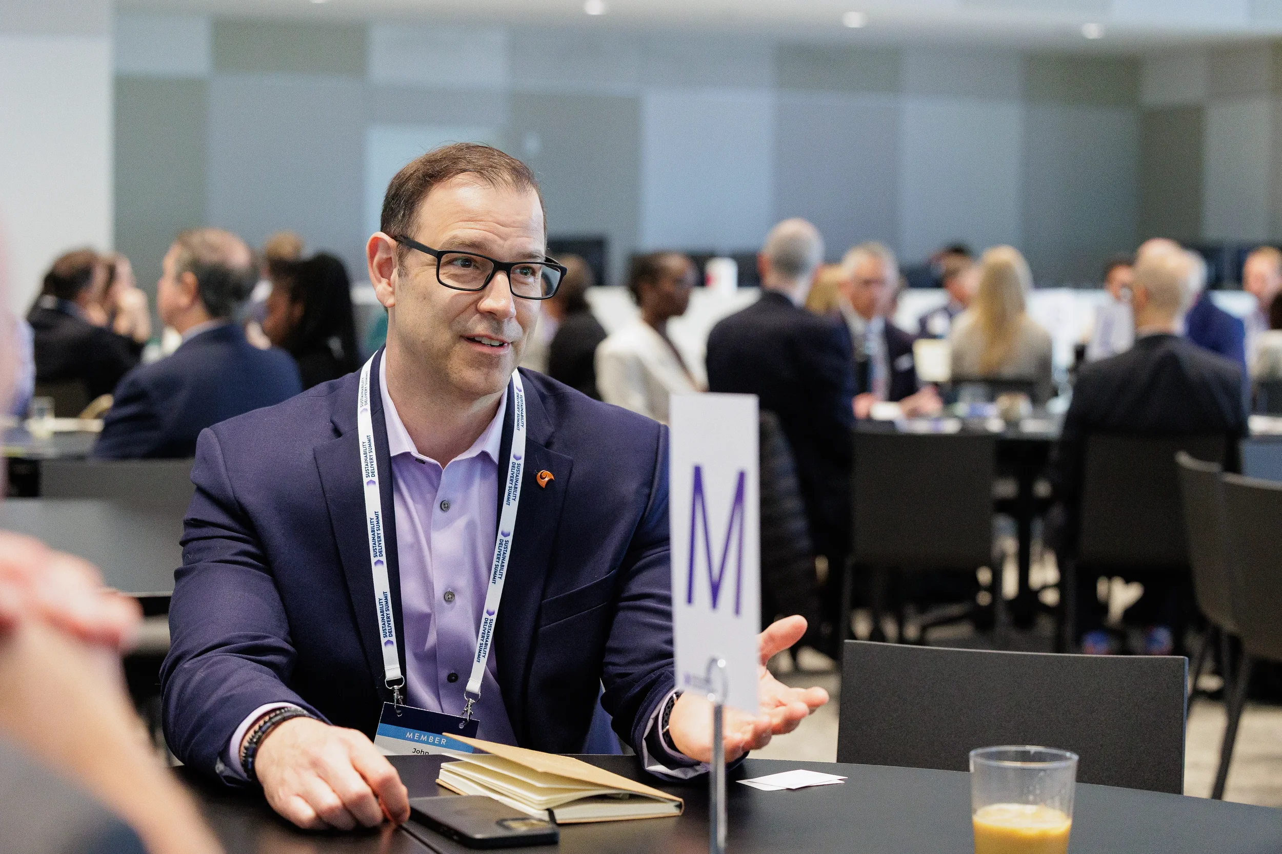 Attendee gestures while speaking at seated table during Chicago industry conference