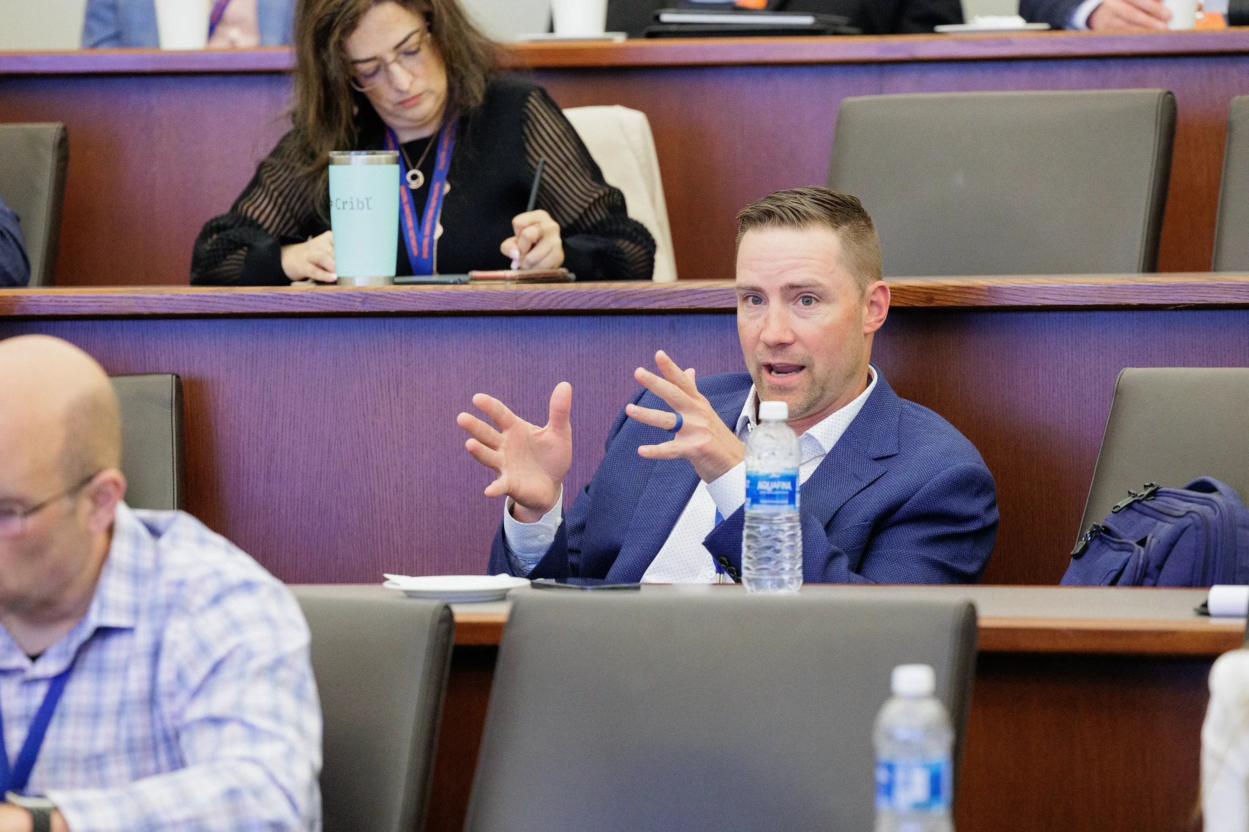 Male attendee with lanyard gestures expressively with both hands during Chicago corporate conference session