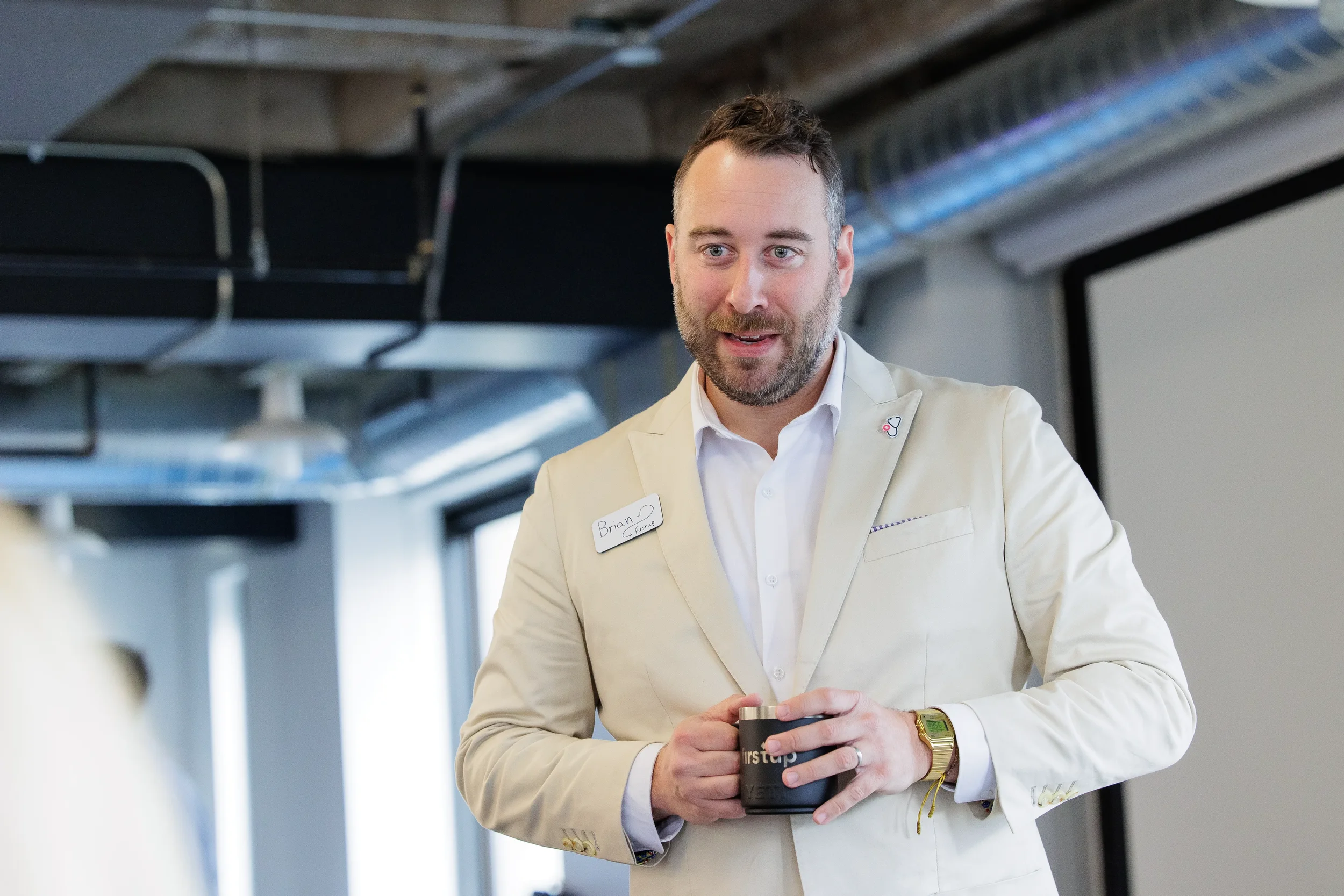 Smiling male attendee holds a branded mug while speaking to a group at Orlando corporate event