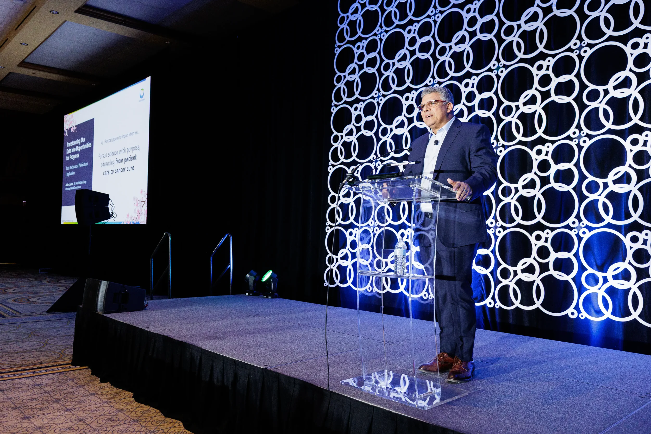 Speaker presents from podium with branded circle backdrop at Orlando industry conference