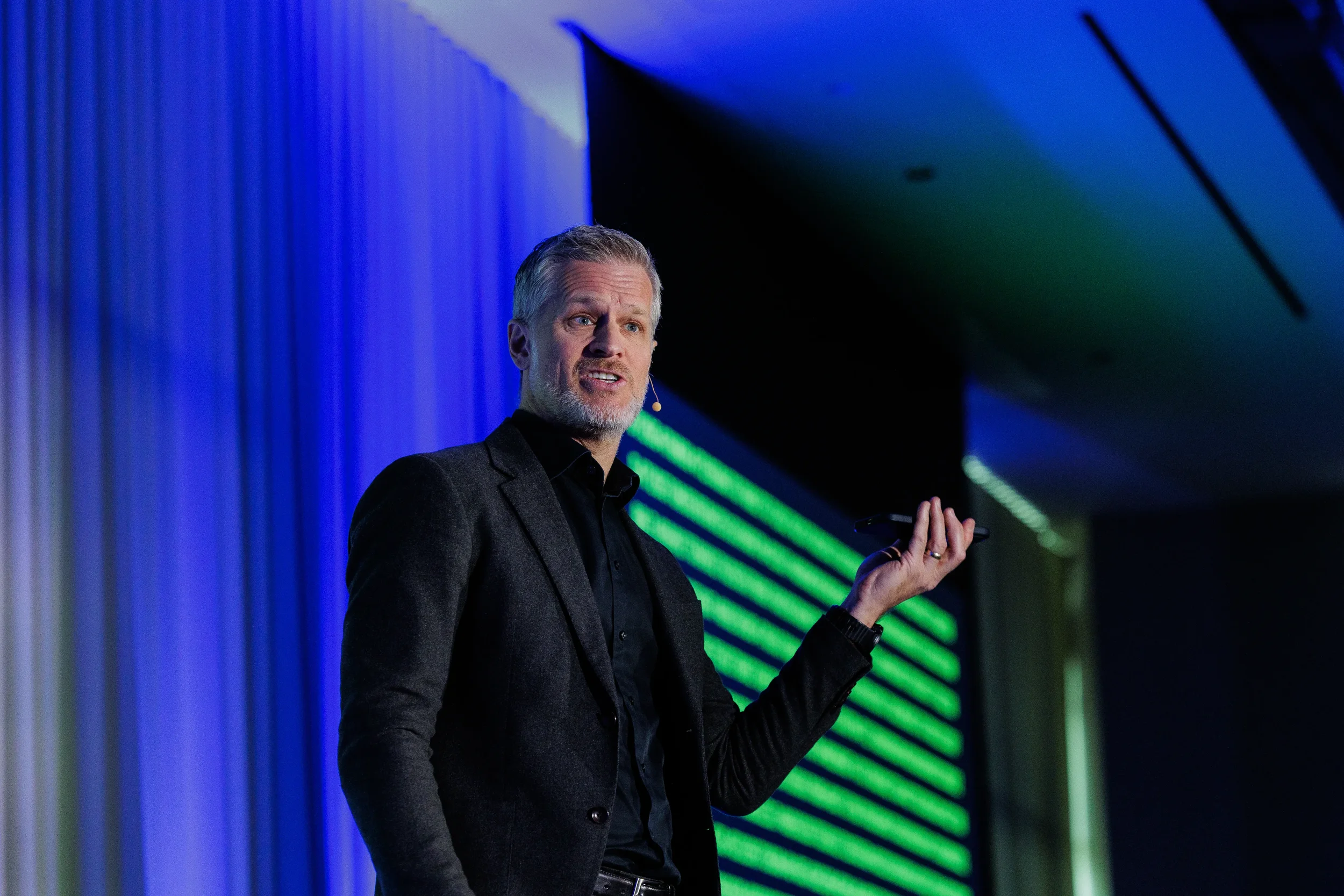 Speaker with headset microphone gestures while holding phone on stage at Orlando industry conference