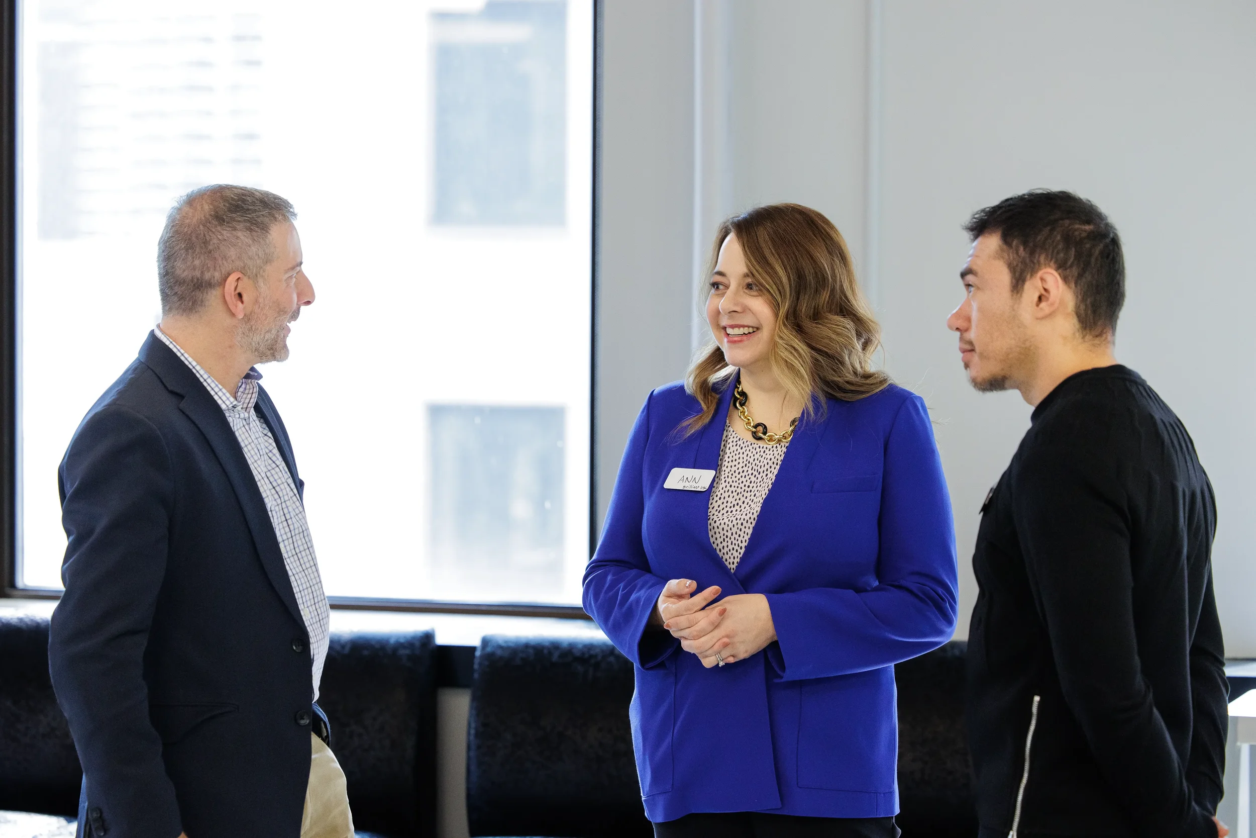 Three attendees share a conversation near bright windows during a networking break at Orlando conference