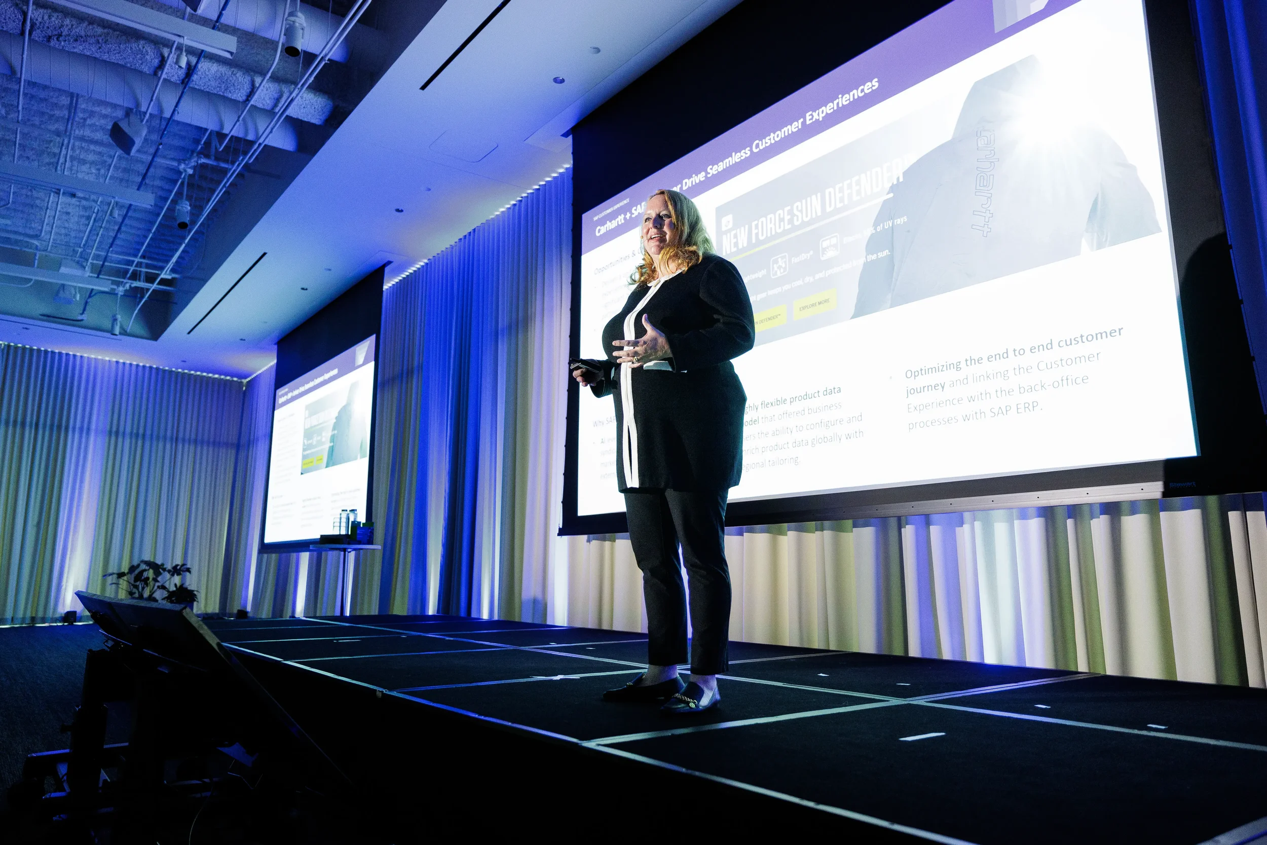Smiling speaker presents beside large projection screen on stage at Chicago industry conference