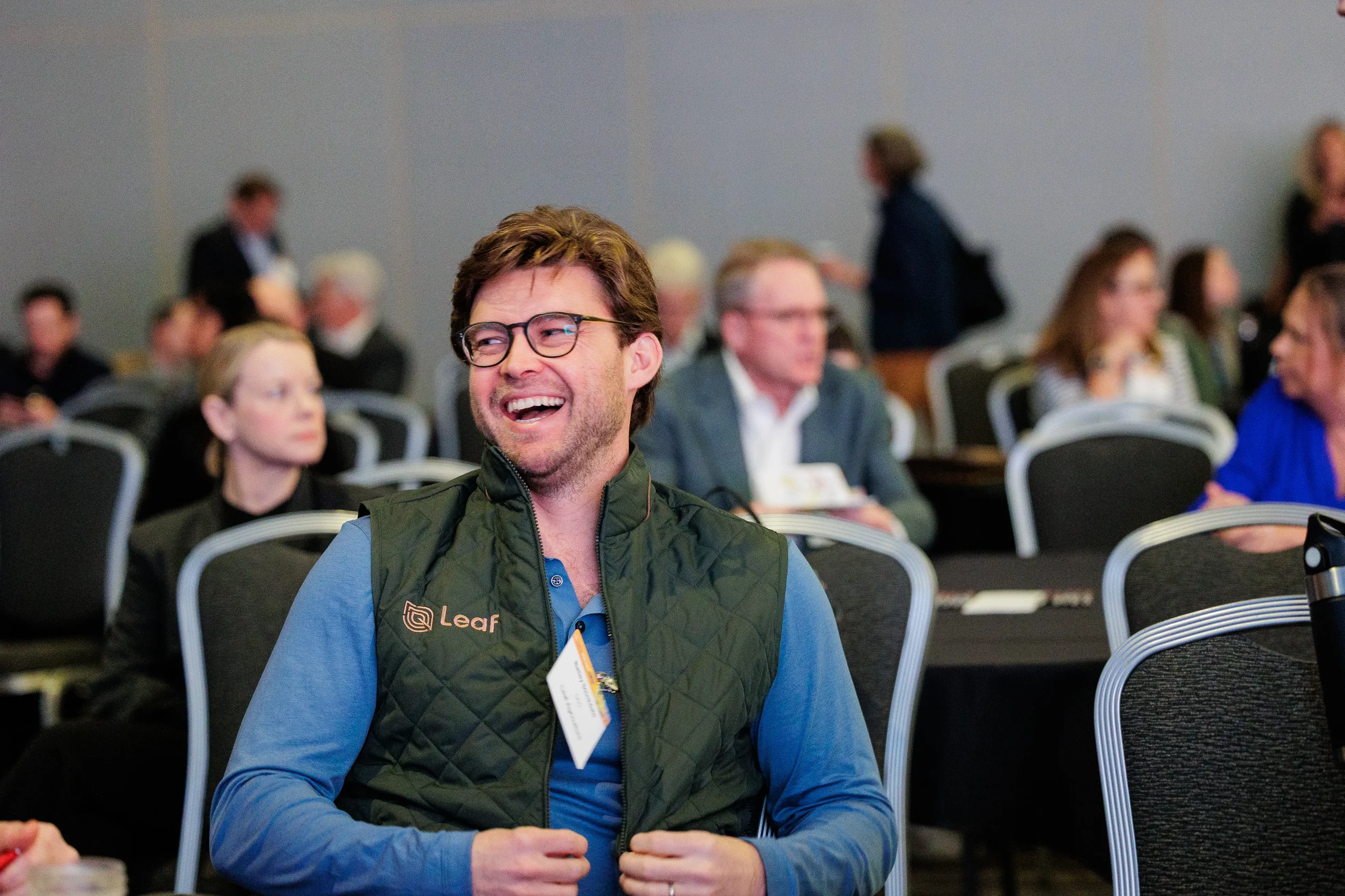 Attendee with name badge laughs while seated during session at Chicago corporate industry conference
